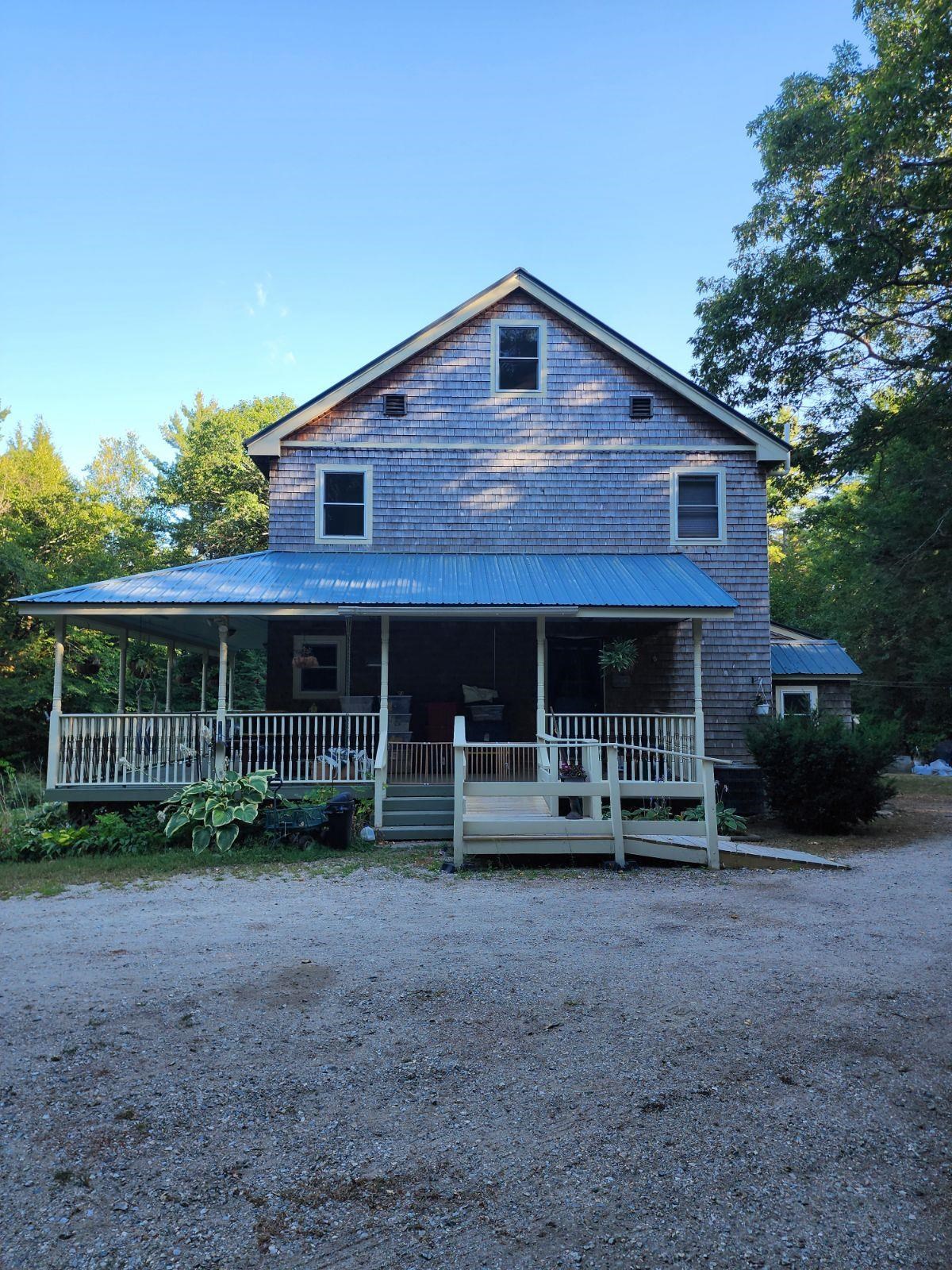 Shingle-sided home with a covered porch and metal roof beside a gravel driveway.