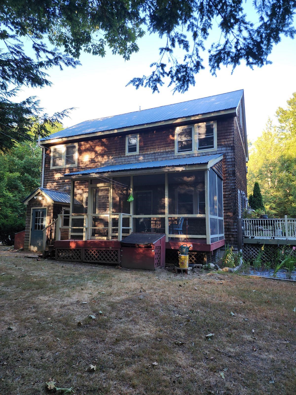 Shingle-sided home with a metal roof and screened porch beneath overhanging trees.