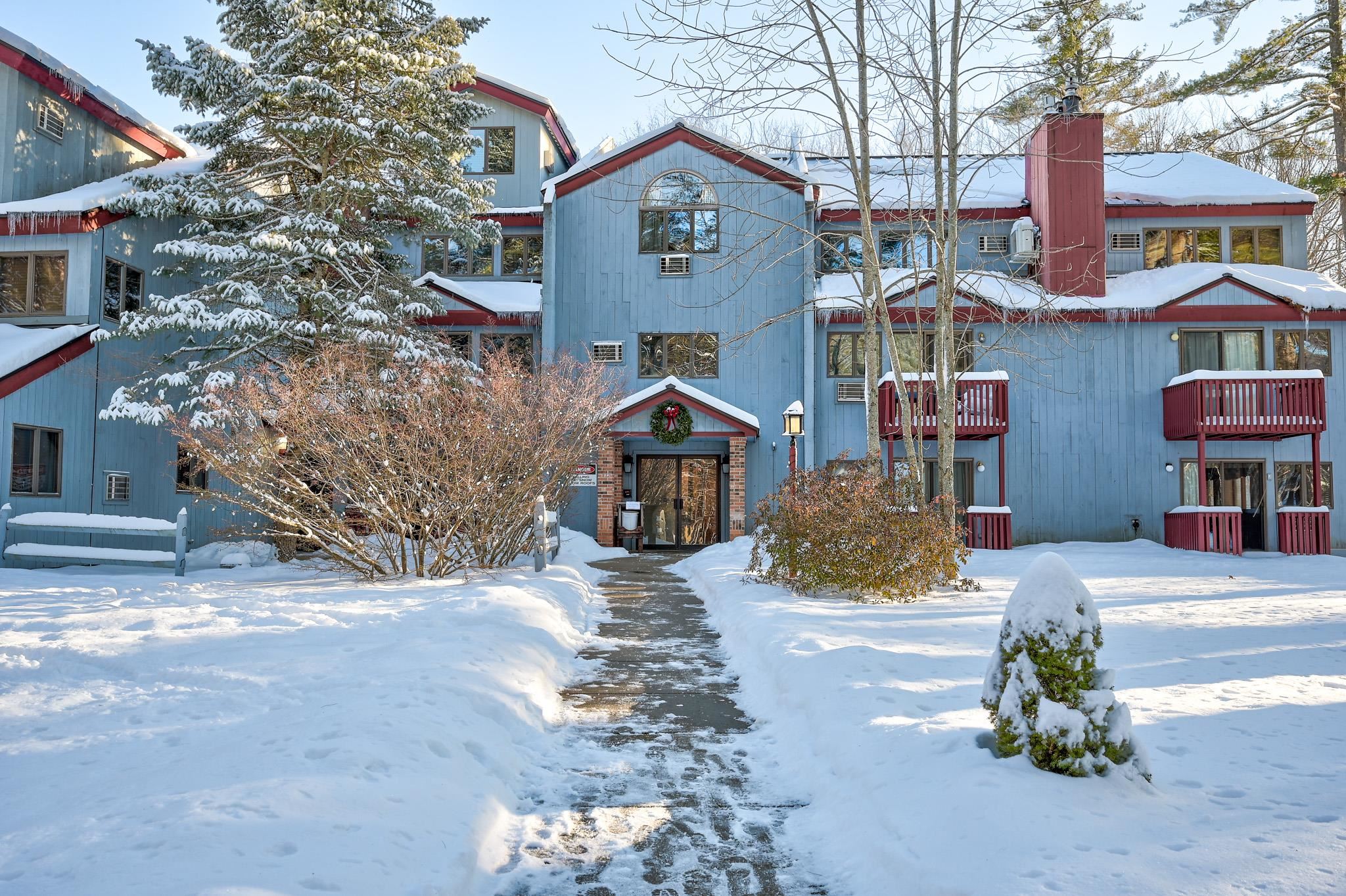 Blue multi-unit building with red trim and balconies, surrounded by snow.
