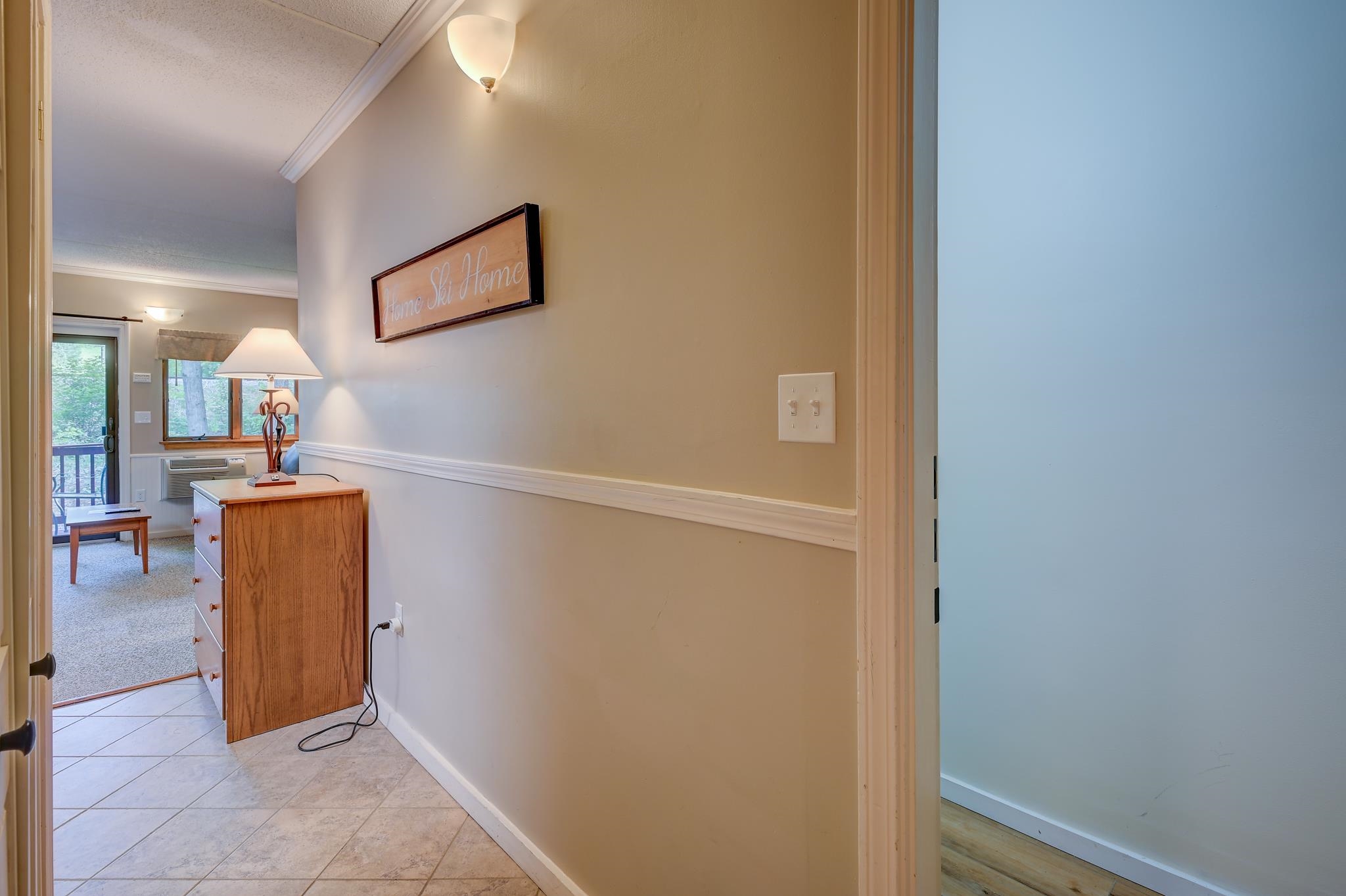 Furnished condo entry with tiled floor, wooden chest, and a view into the carpeted living area.