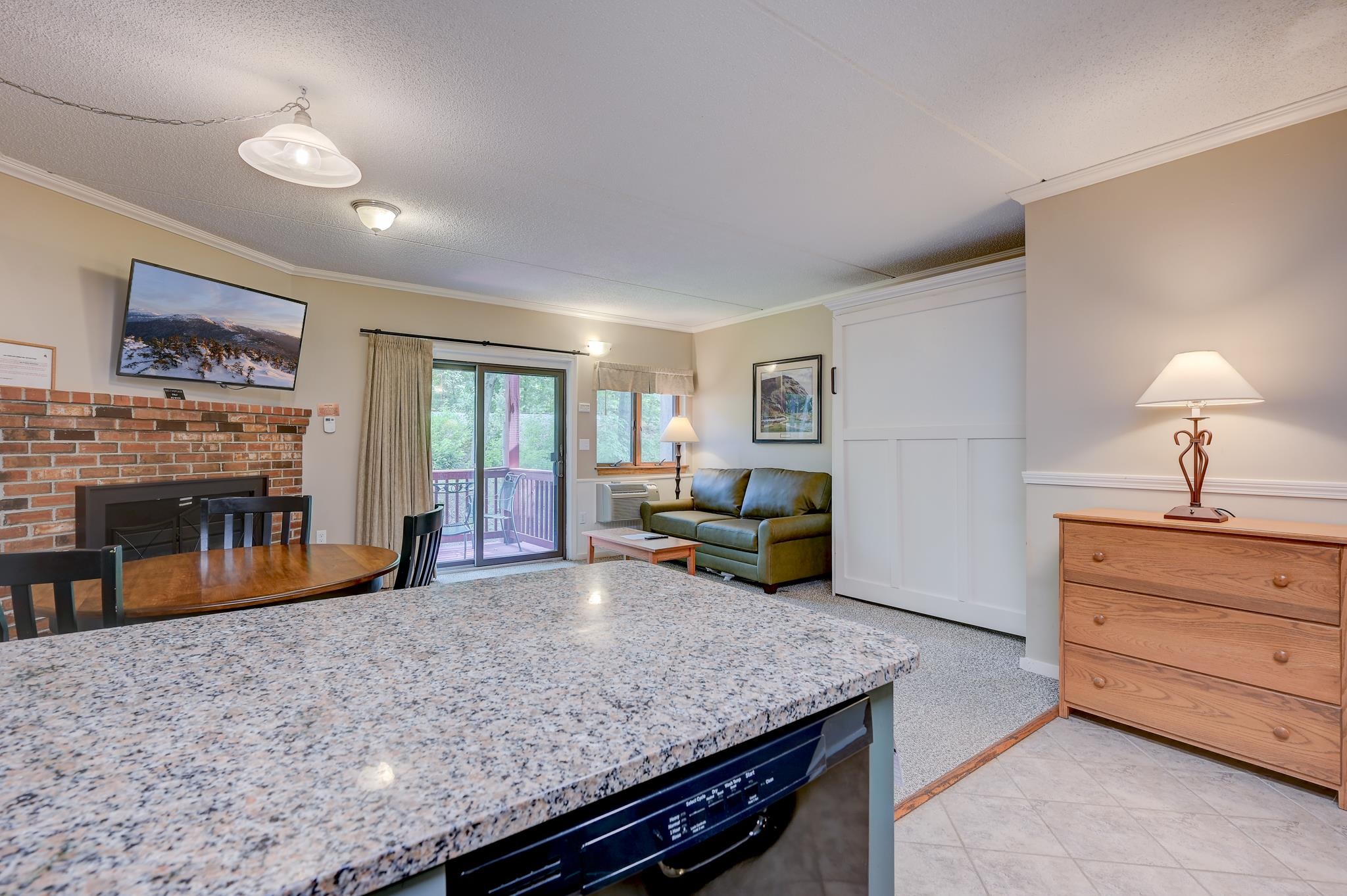 Open-plan living and dining area with a brick fireplace, green sofa, and sliding door to a deck.