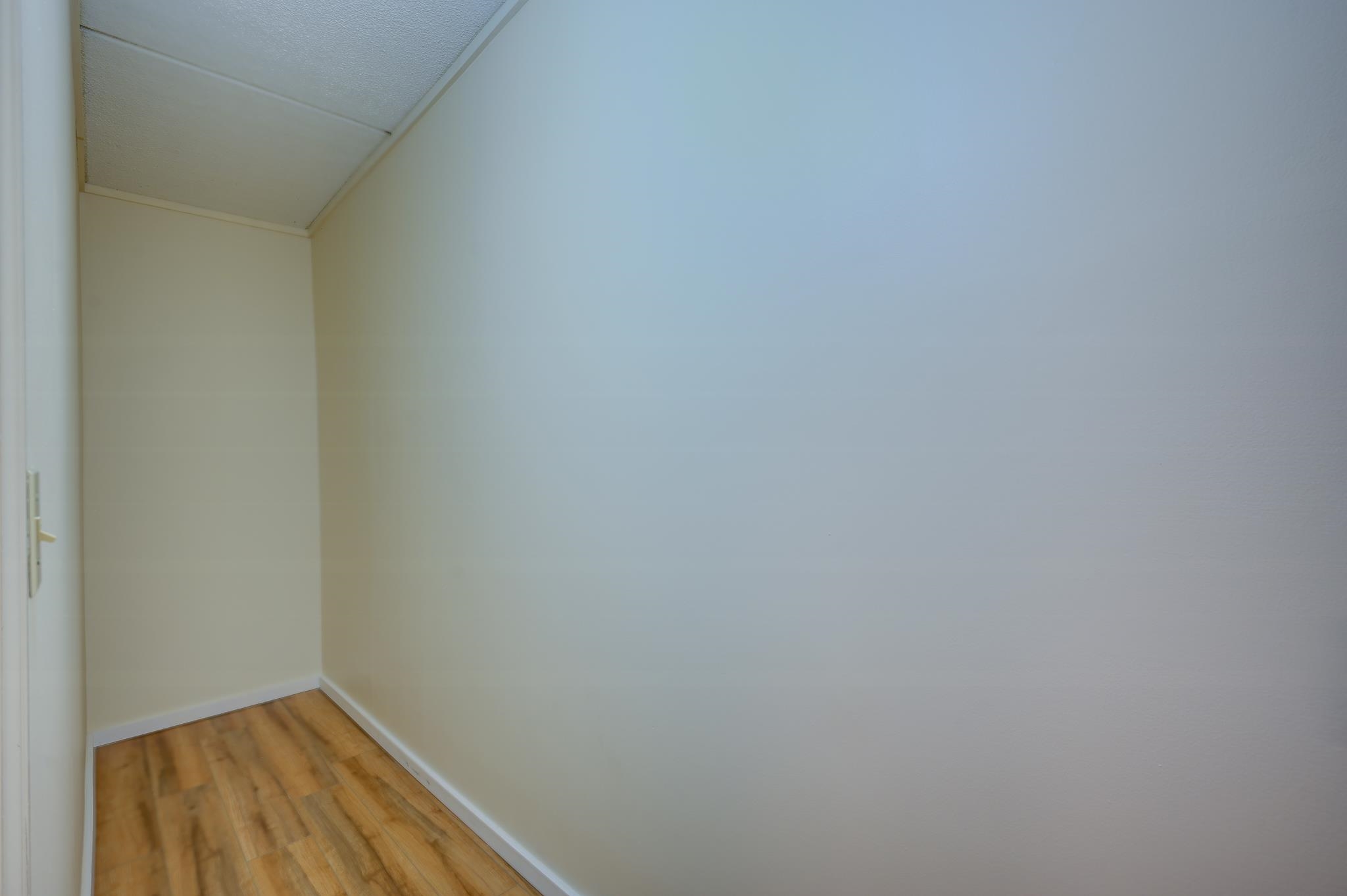 Empty narrow room with white walls and wood-look flooring.