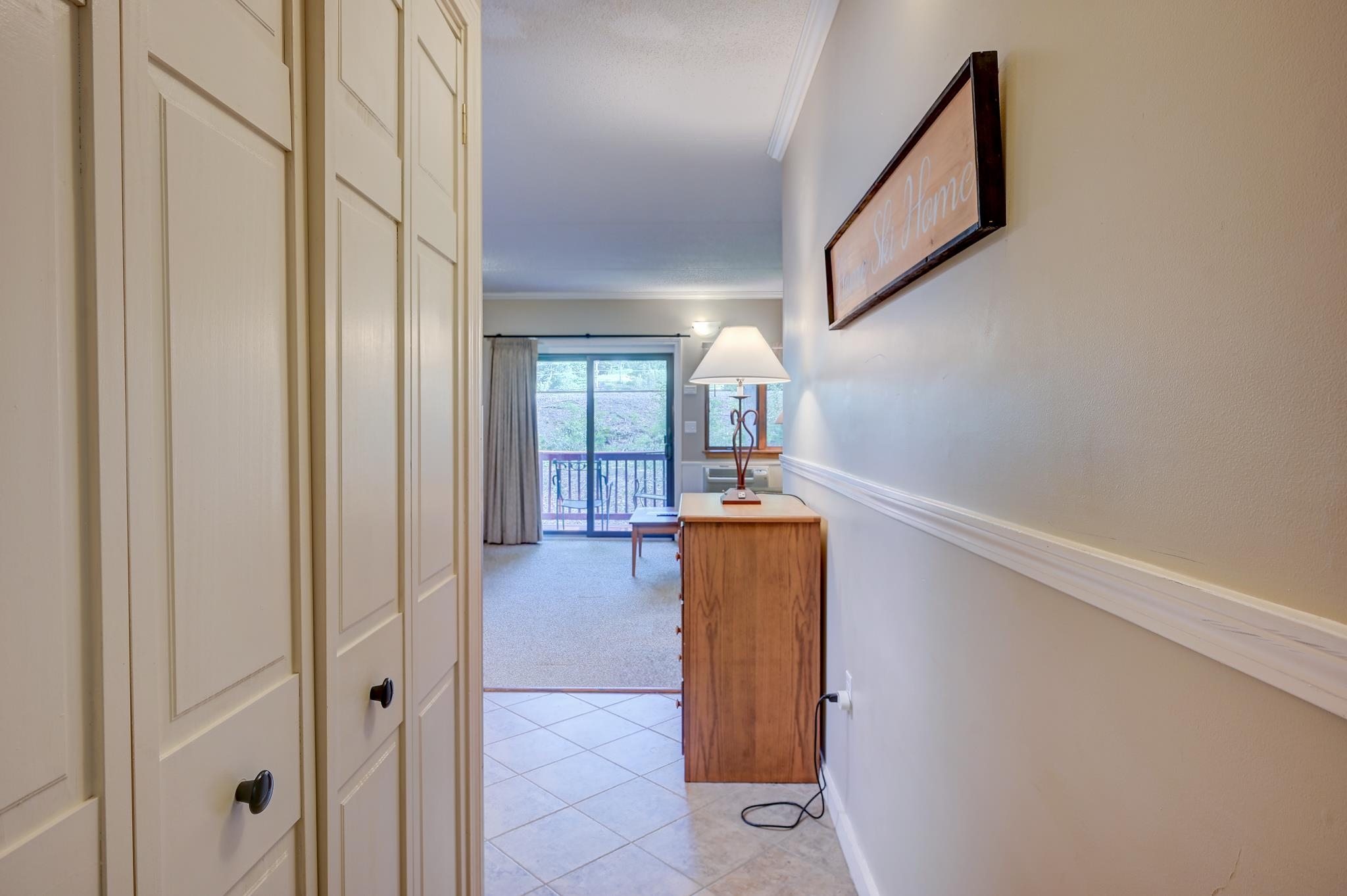 Condo hallway with built-in cabinets leading to a room with a dresser and balcony doors.