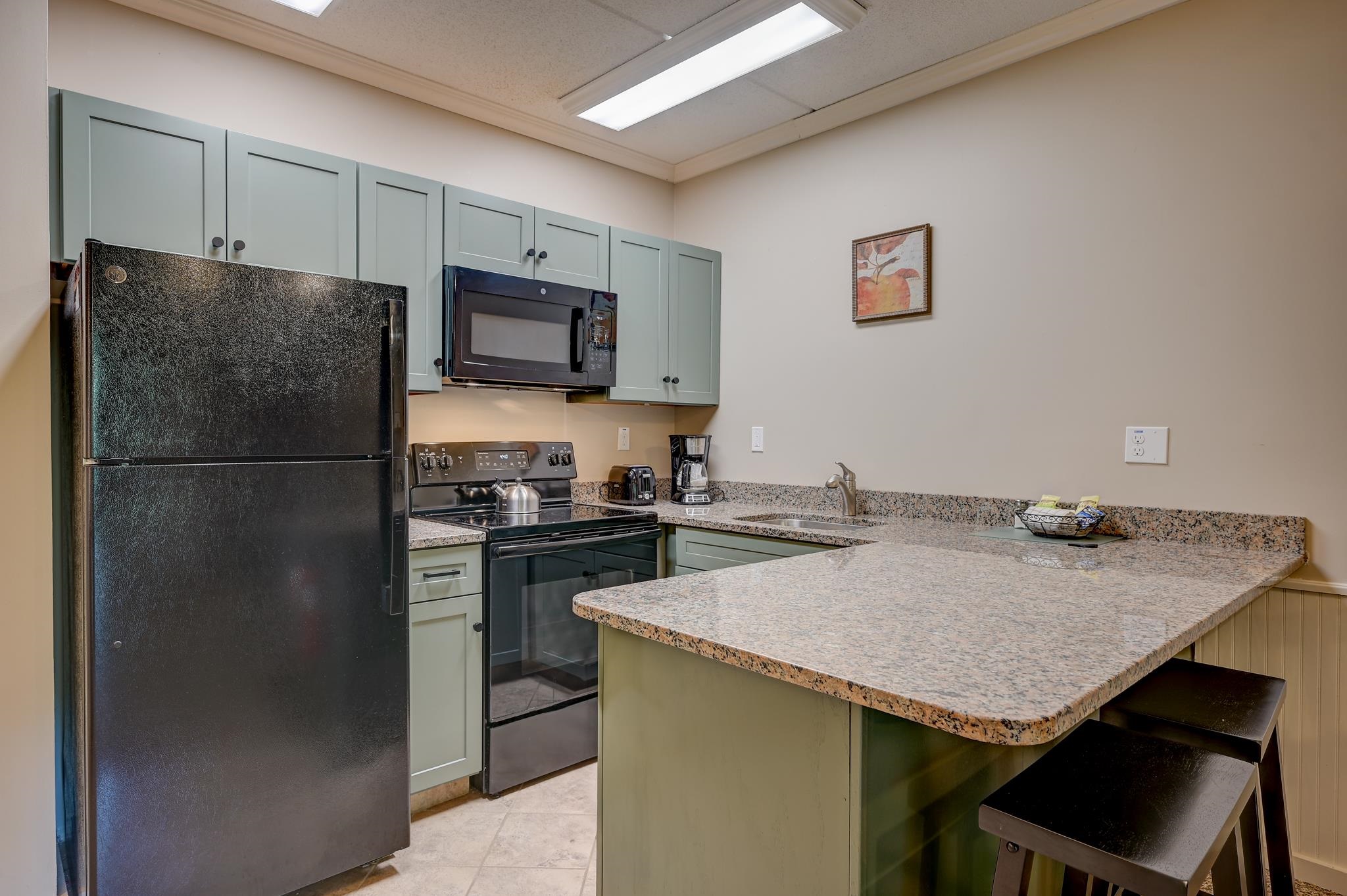Kitchen with pale green cabinets, black appliances, granite counters, and a peninsula with stools.