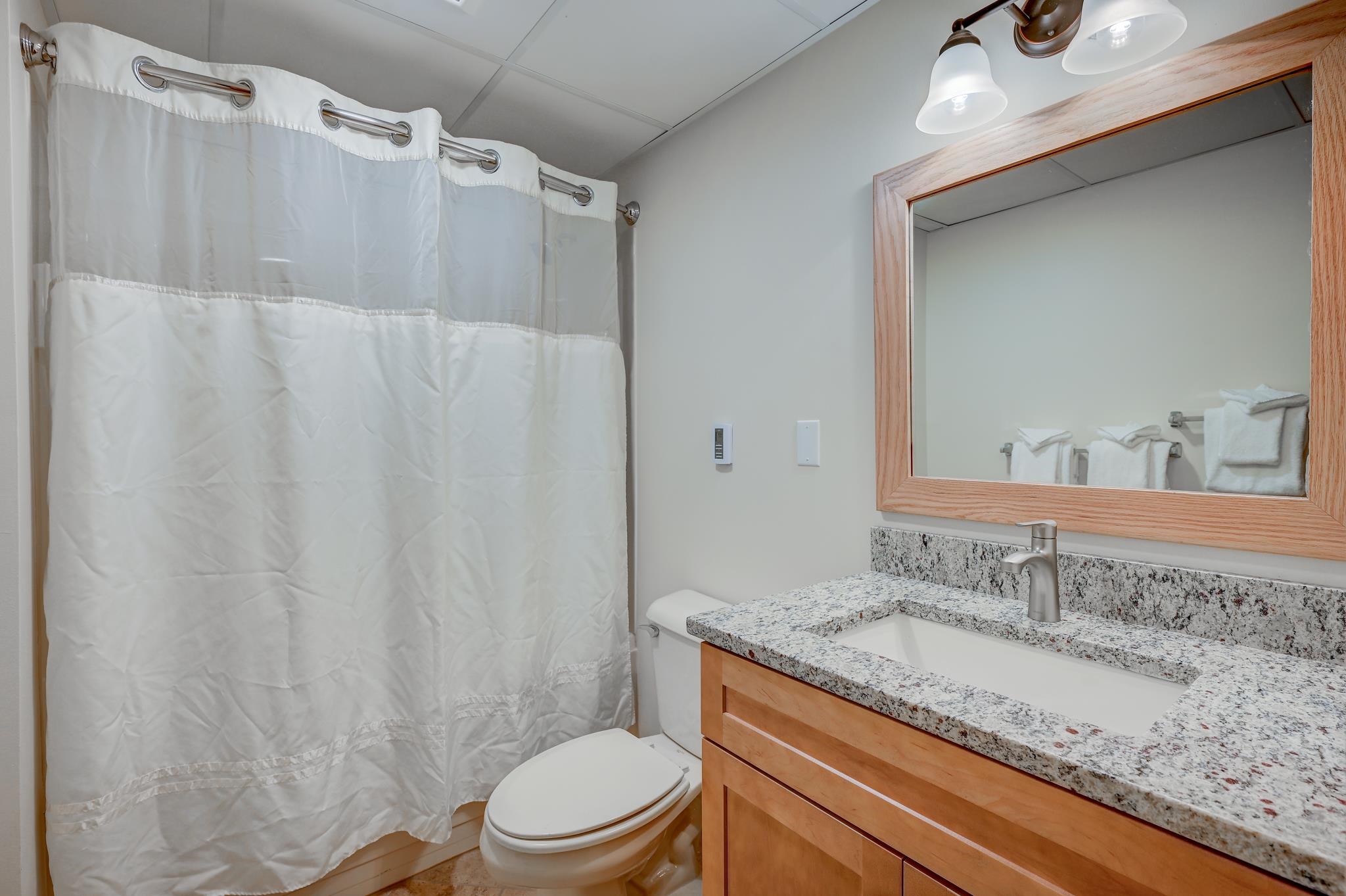 Bathroom with a white shower curtain, granite vanity, wood cabinetry, and a large framed mirror.