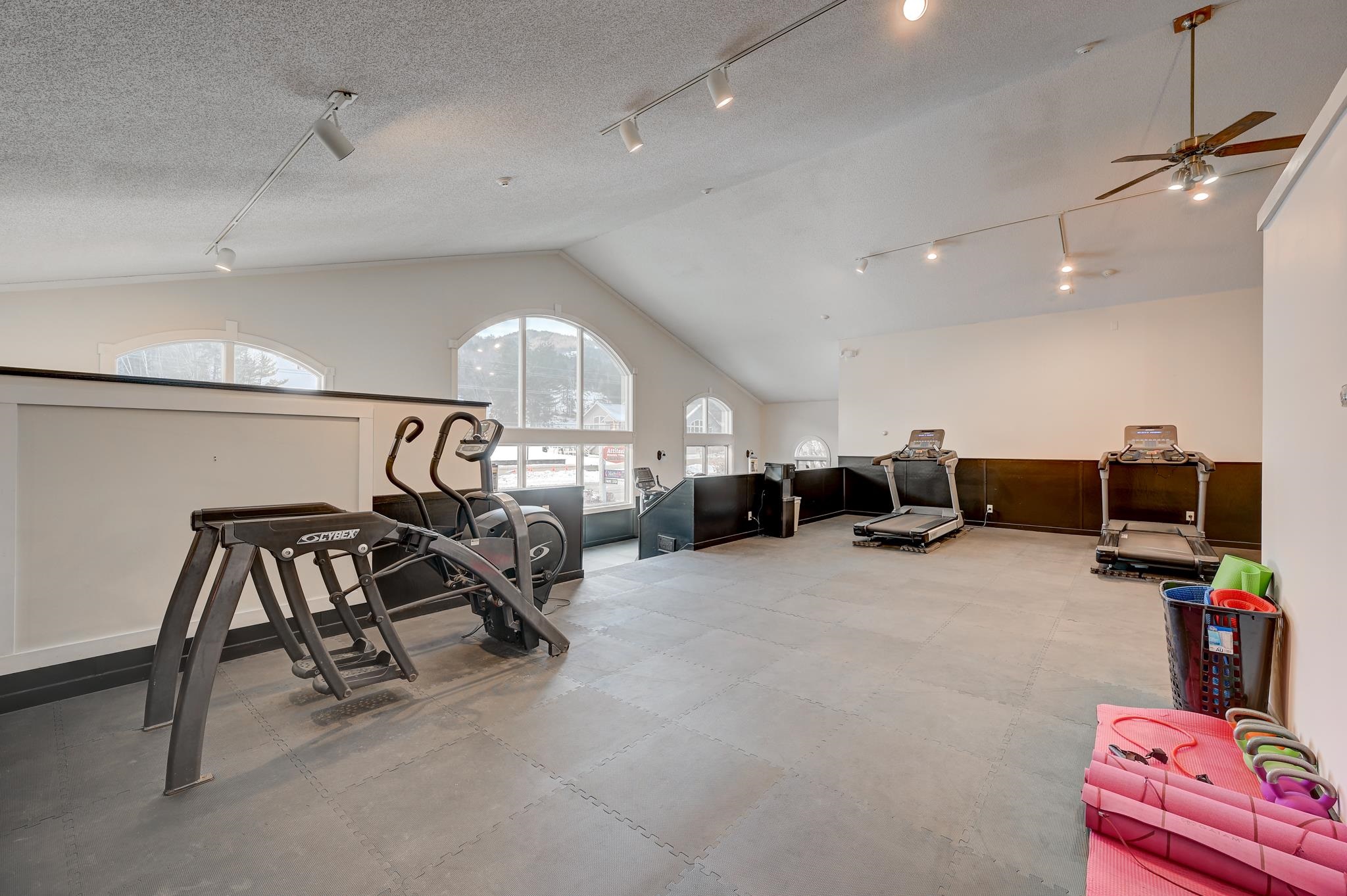 Fitness room with treadmills and elliptical machines beneath tall arched windows.