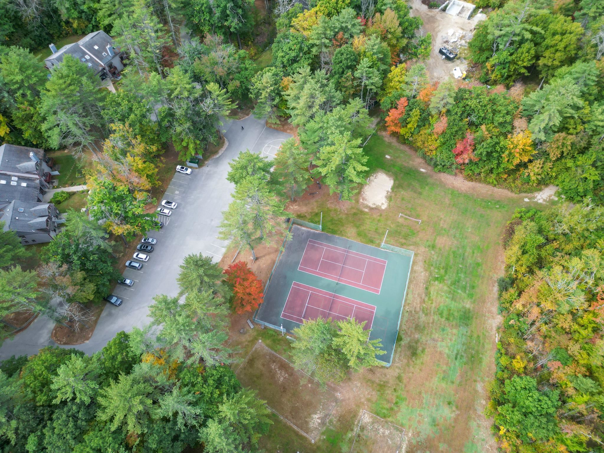 Aerial view of a wooded community with tennis courts, parking, and open grassy recreation areas.