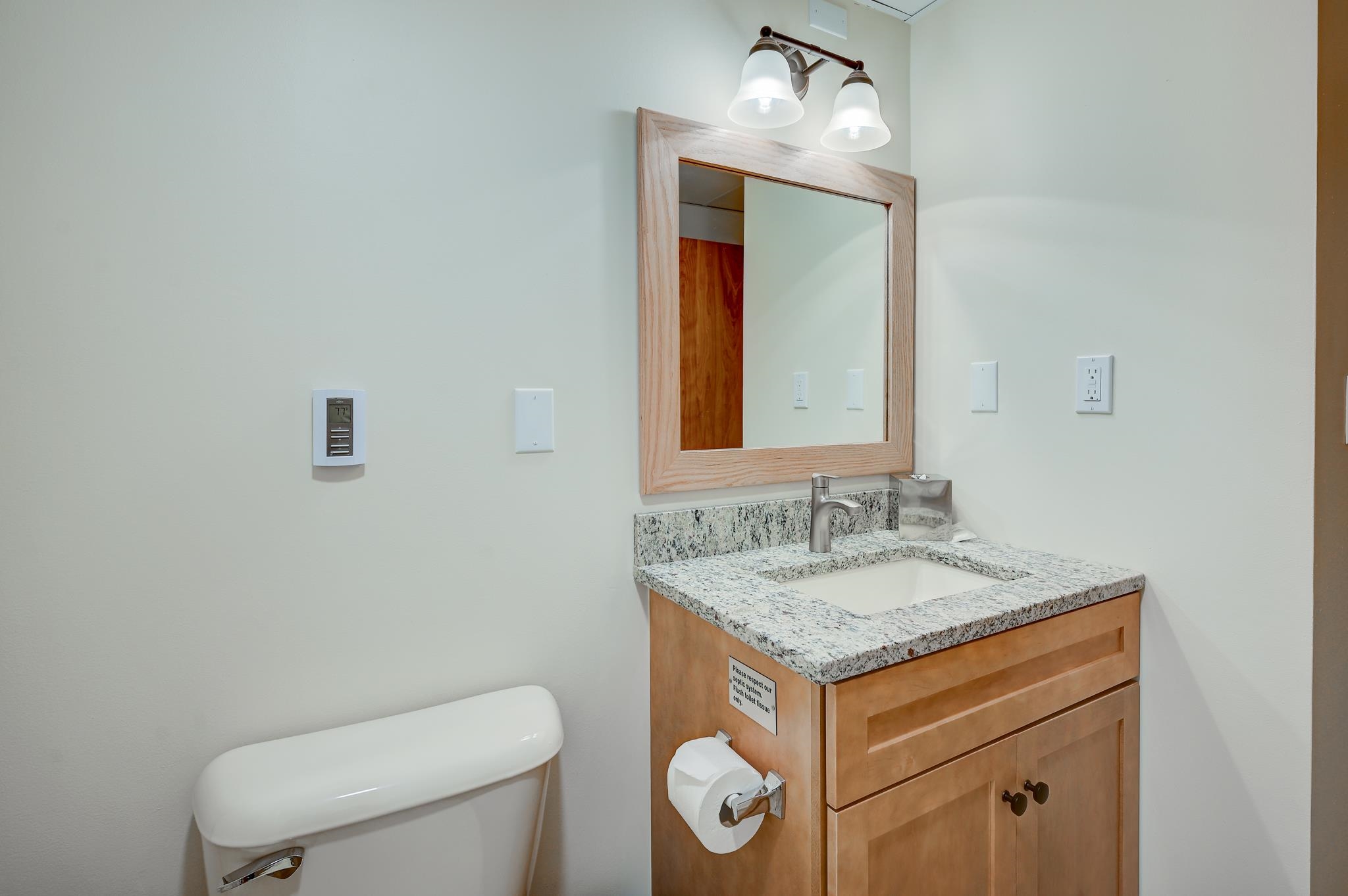 Bathroom with a wood vanity, granite countertop, framed mirror, and toilet.