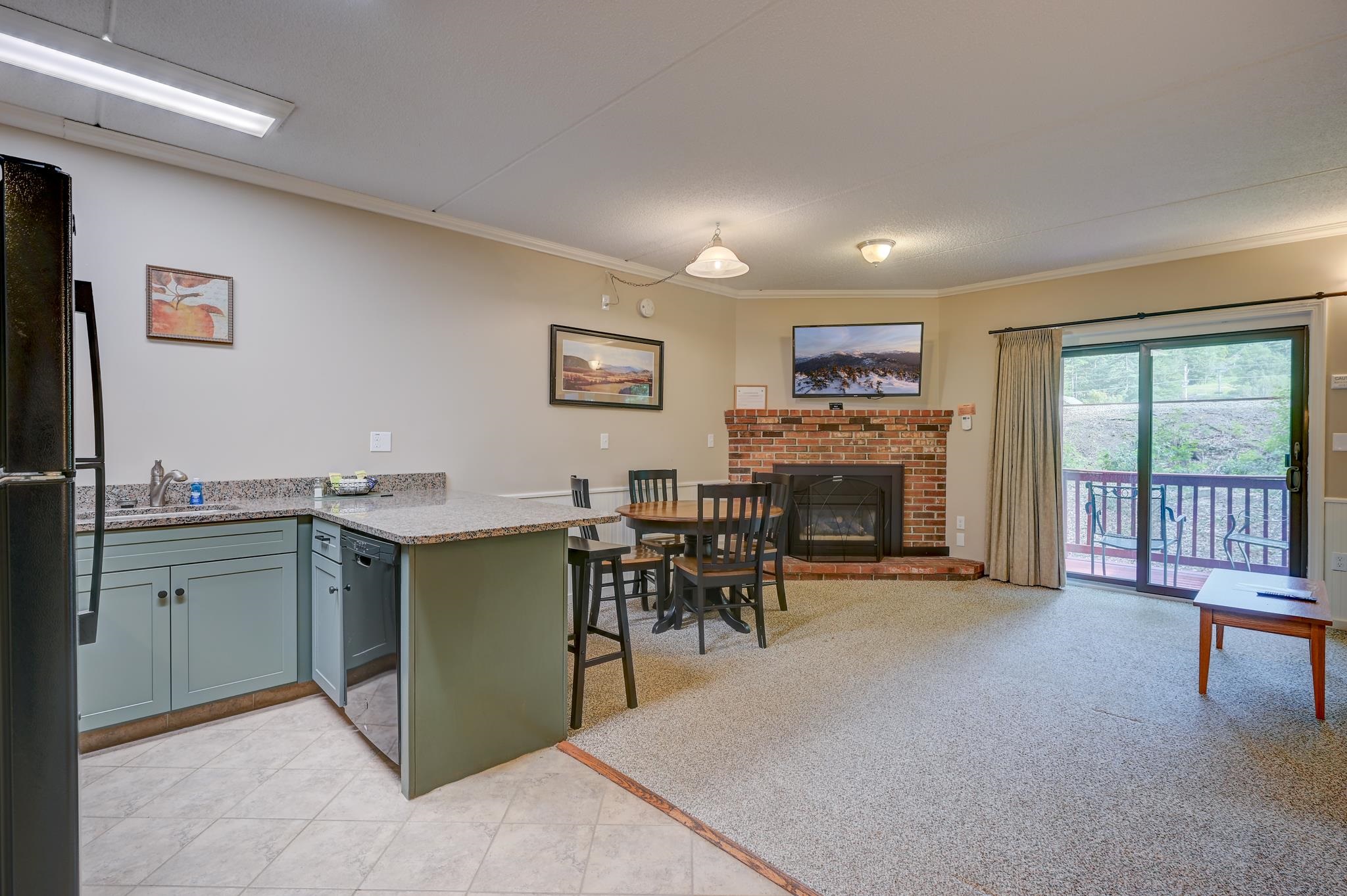 Open-plan kitchen and living area with a brick fireplace and sliding door to a deck.