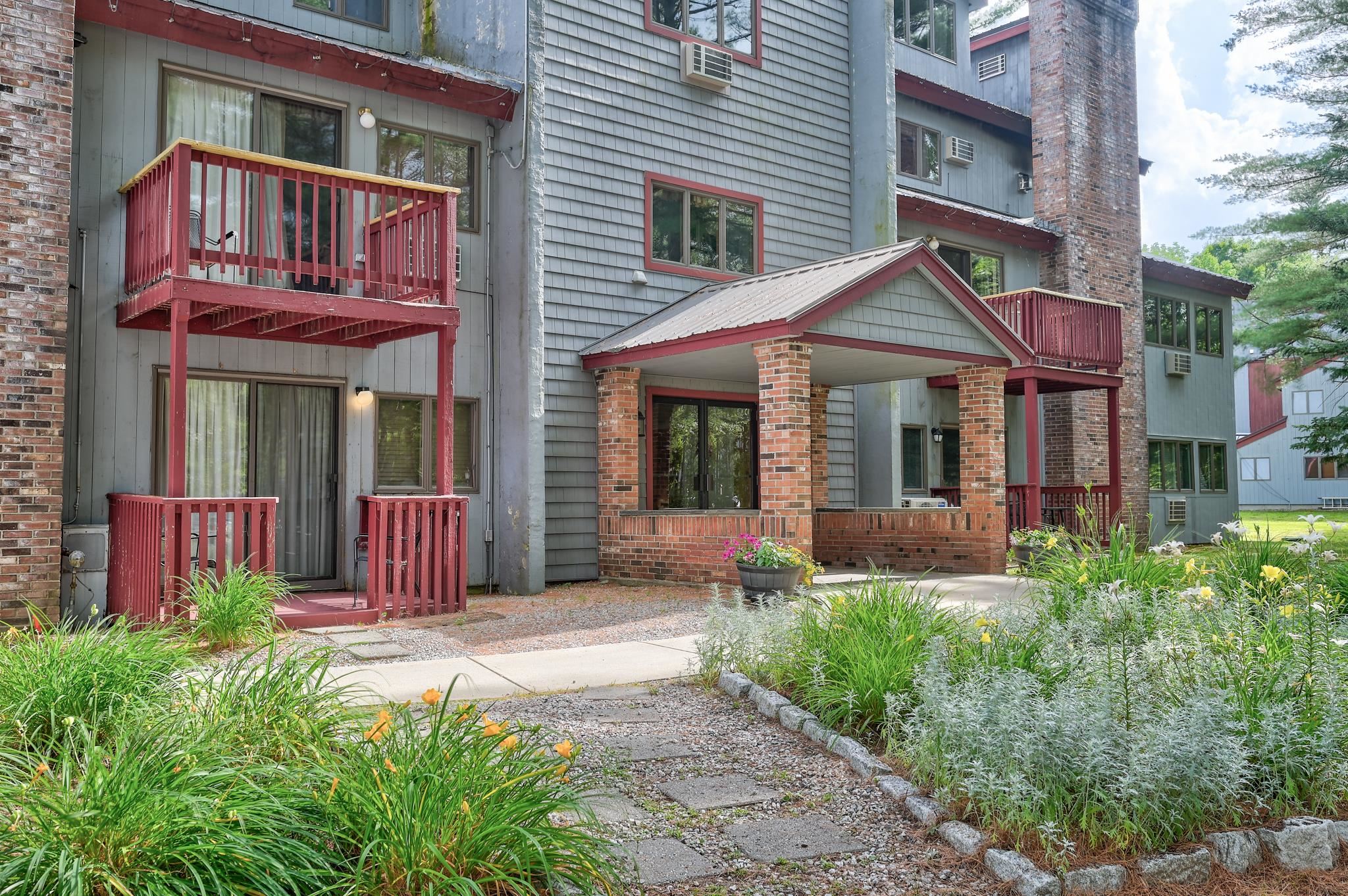 Residential building with red-railed balconies, a covered brick entrance, and landscaped flower beds.