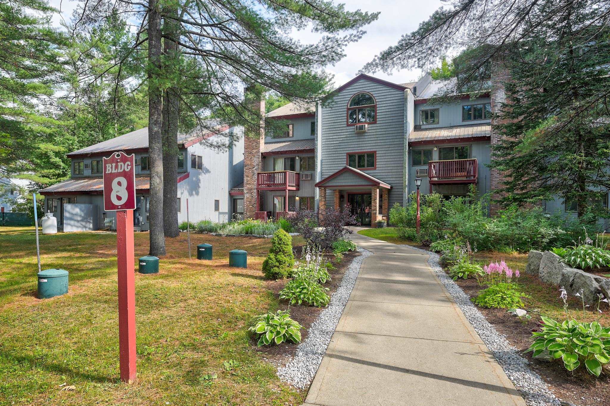 Condominium building marked BLDG 8, with balconies and a landscaped walkway to the entrance.