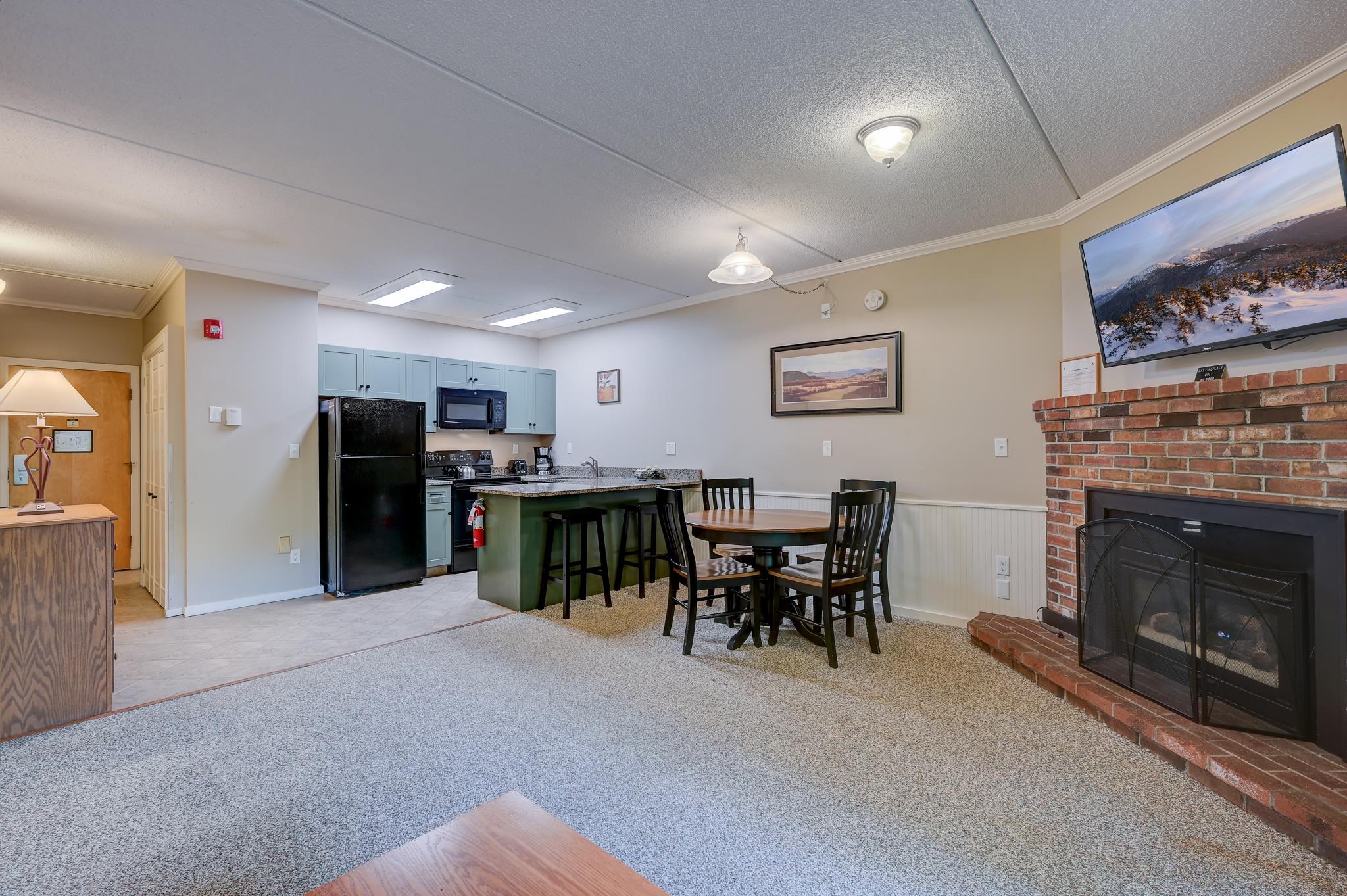 Open-plan condo kitchen and dining area with blue cabinets, a breakfast bar, and a brick fireplace.