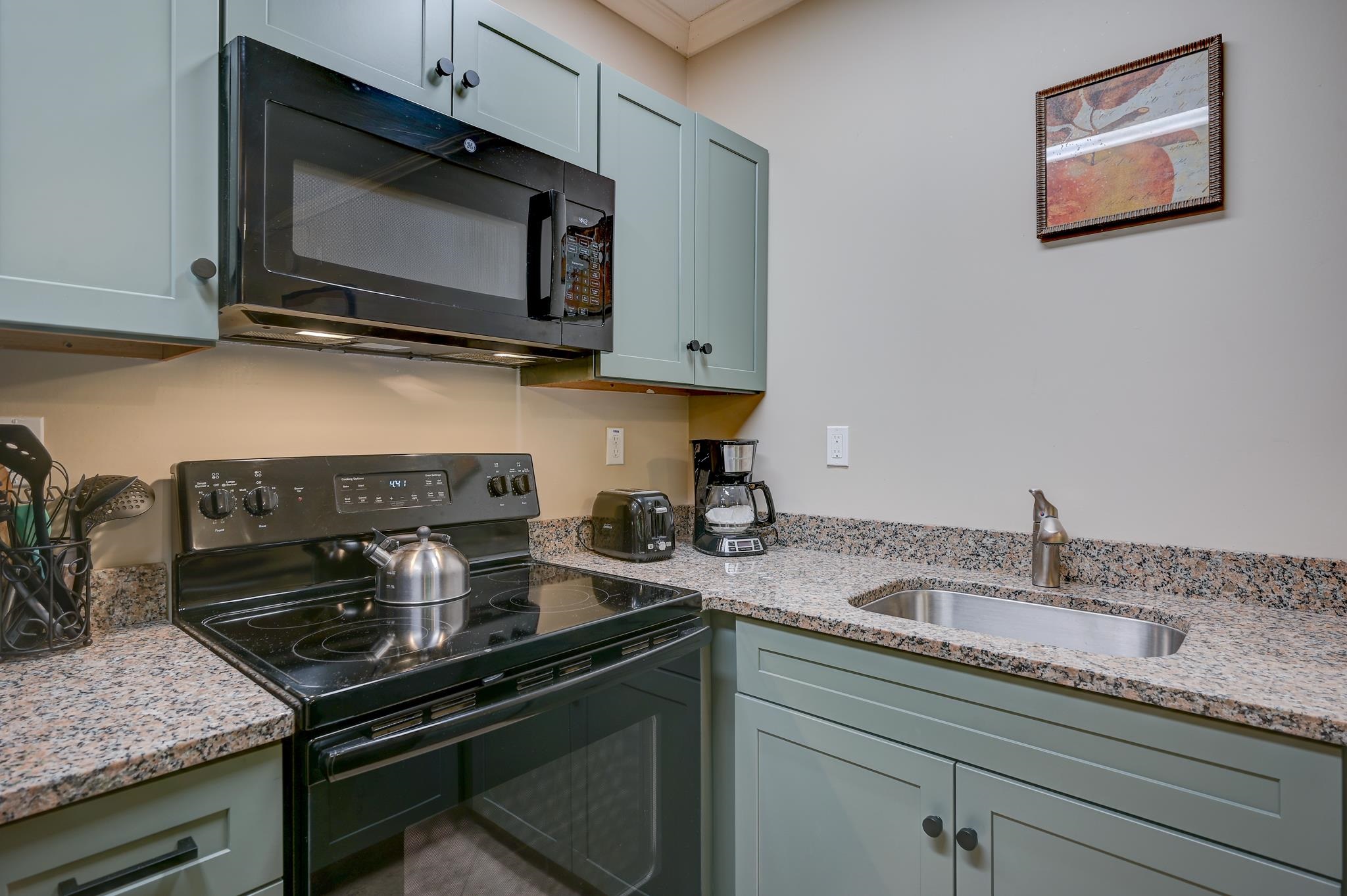 Kitchen with pale green cabinets, granite counters, black range and microwave, and a stainless steel sink.