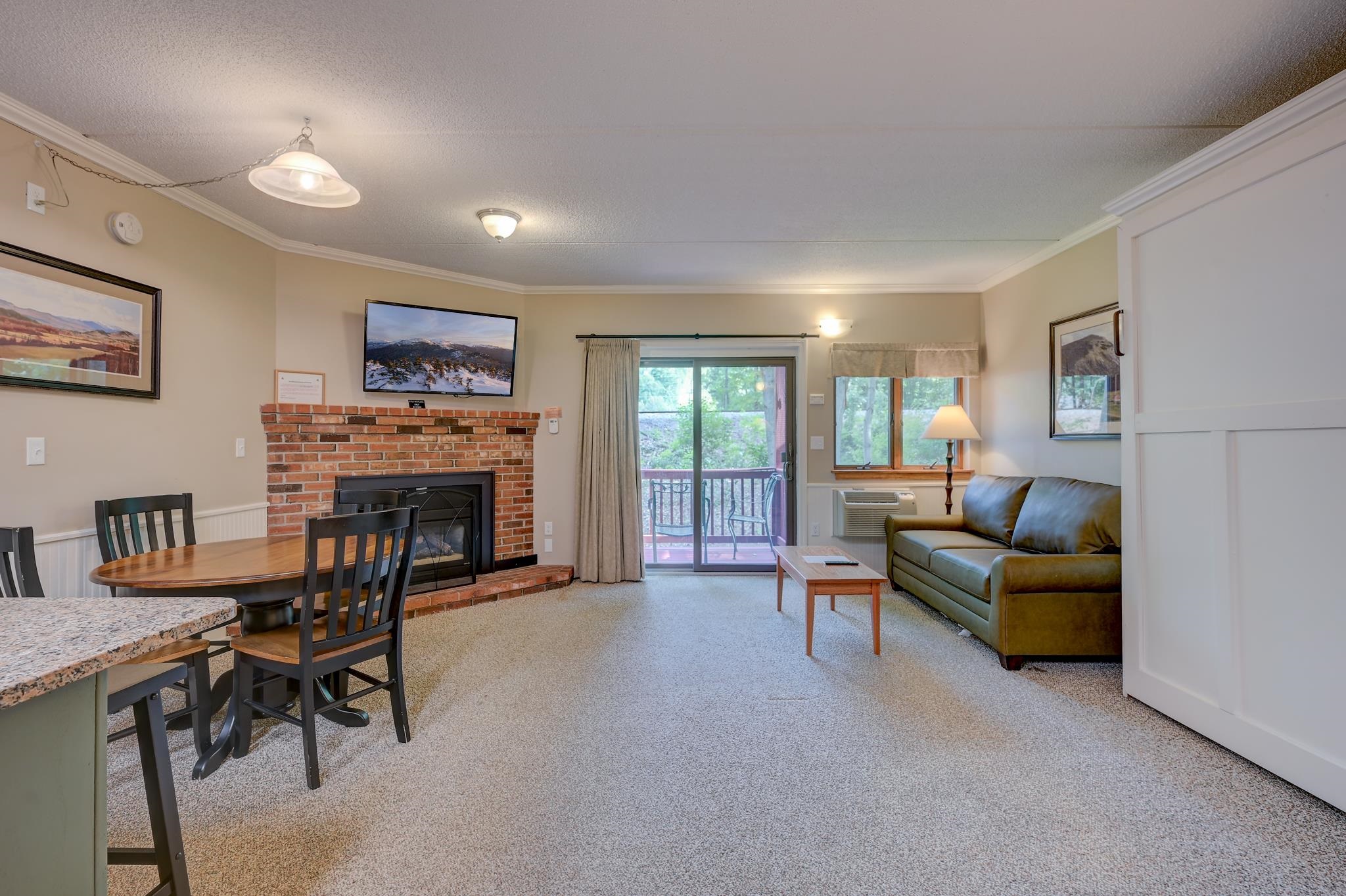 Living and dining room with a brick fireplace, leather sofa, and sliding glass doors to a balcony.