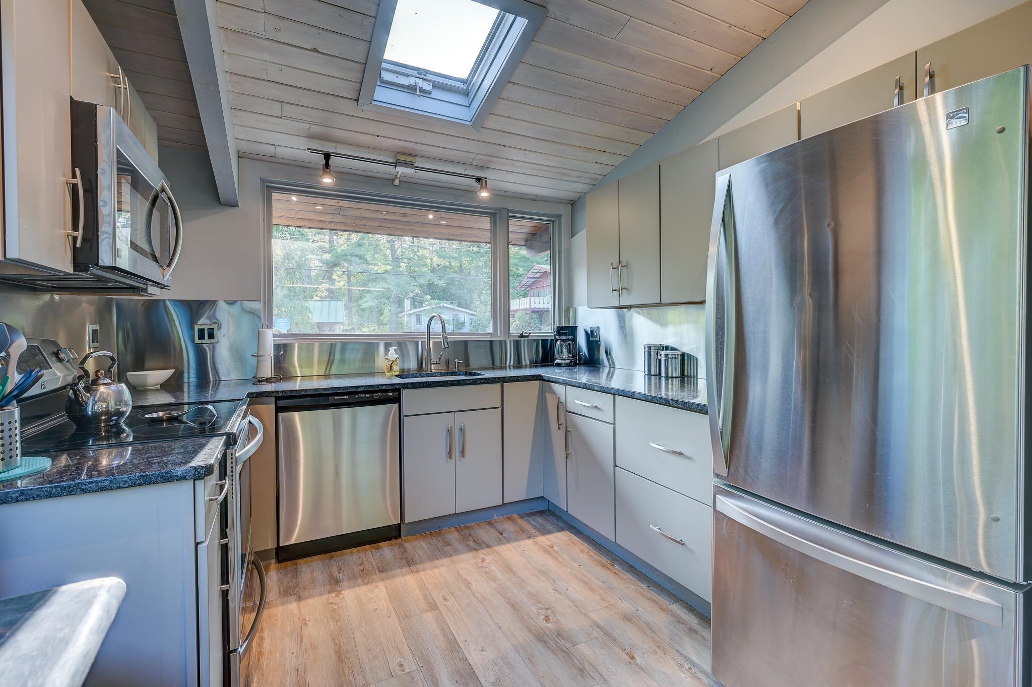 Modern kitchen with stainless steel appliances, a skylight, and a wide window above the sink.