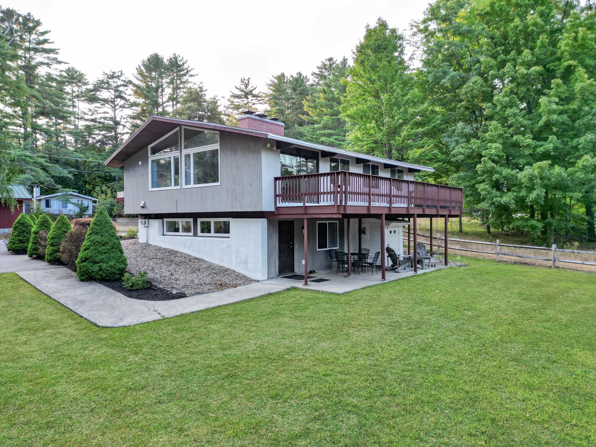 Split-level home with a raised deck and covered patio, surrounded by lawn and mature trees.