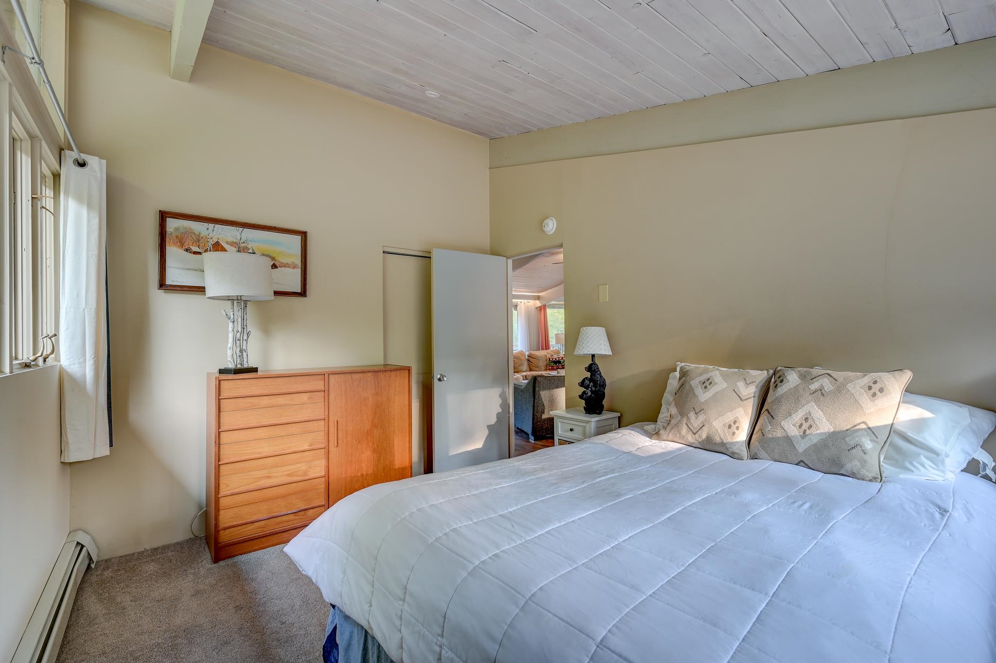 Furnished bedroom with a white quilted bed, patterned pillows, and a wooden dresser beside the window.