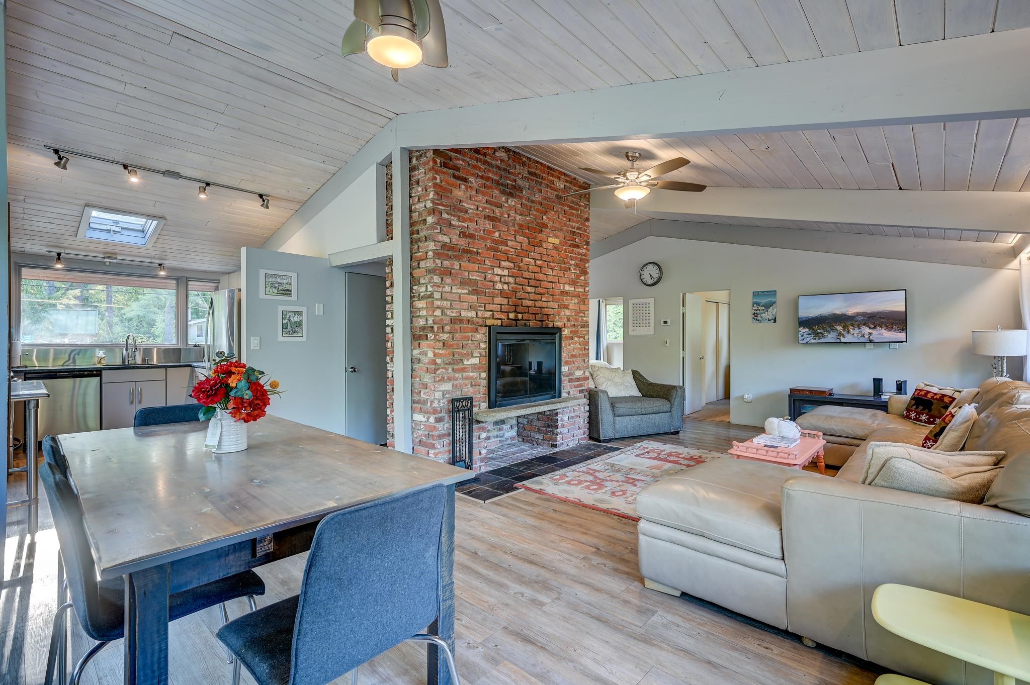 Open-plan living and dining area with a tall brick fireplace, vaulted ceiling, and skylight.