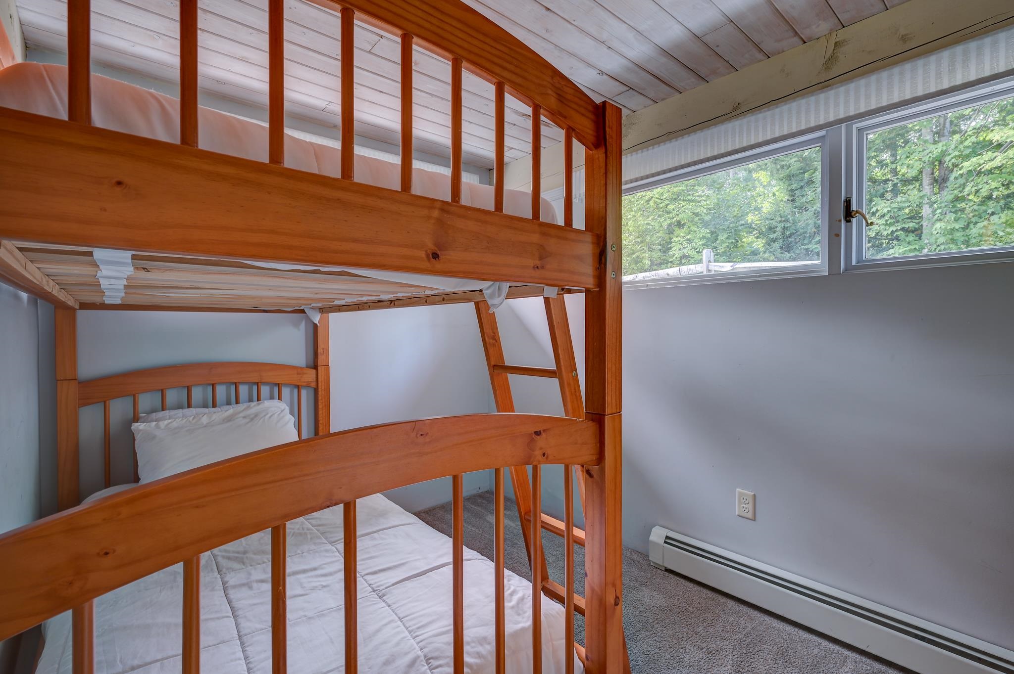 Bedroom with a wooden bunk bed, white bedding, and a wide window overlooking trees.
