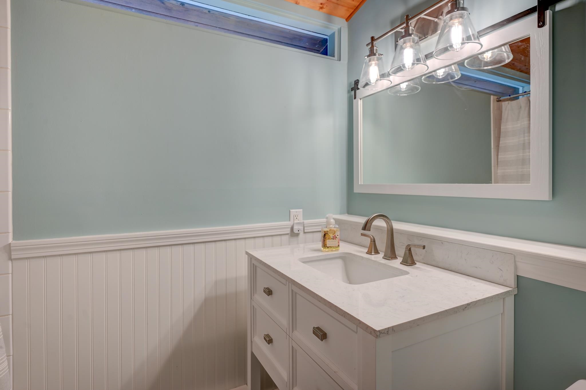 Bathroom vanity with a marble-look counter, bronze faucet, framed mirror, and pale blue walls.