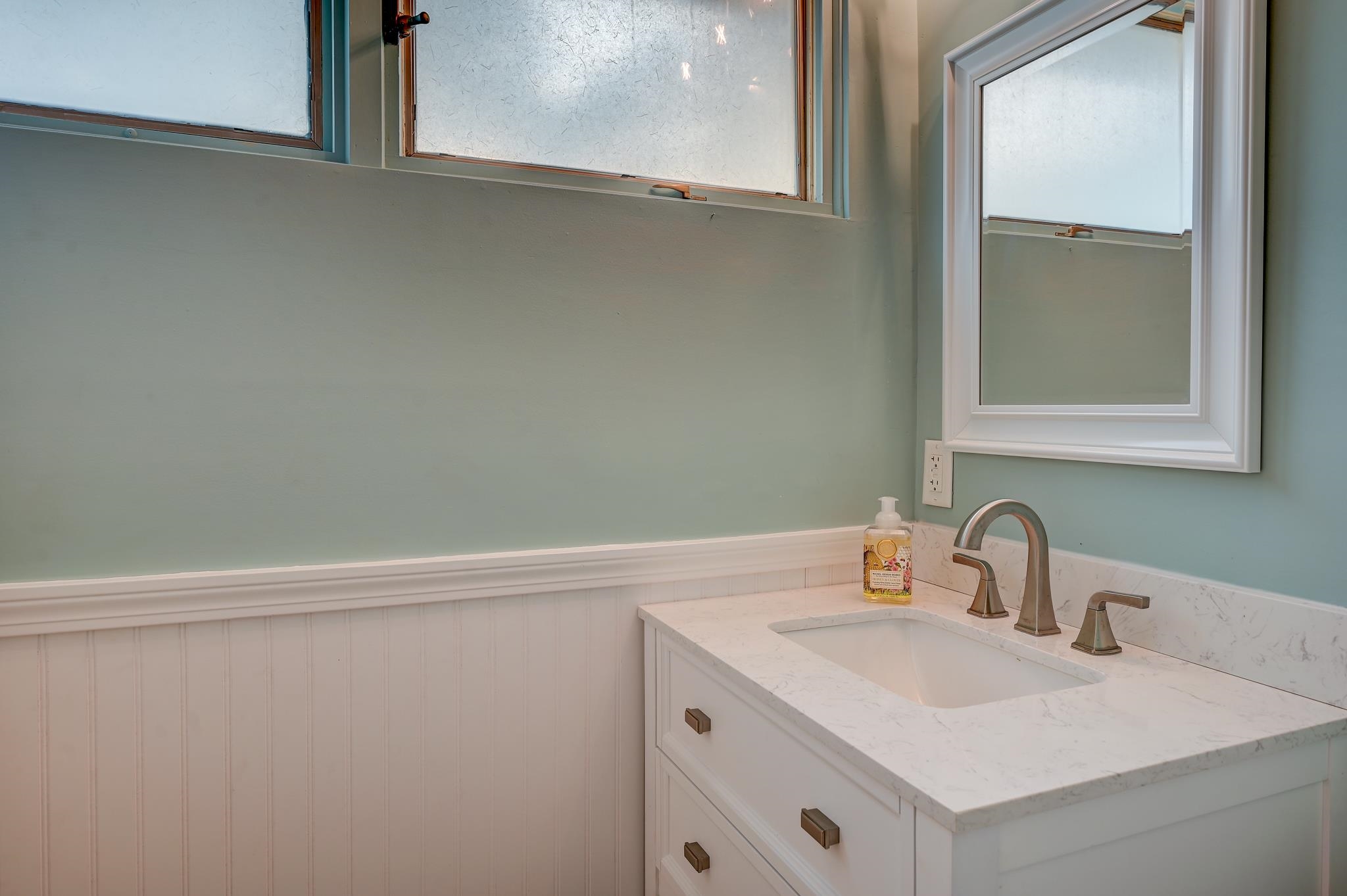 Bathroom vanity with a white sink, marble-look countertop, brushed-metal faucet, and framed mirror.