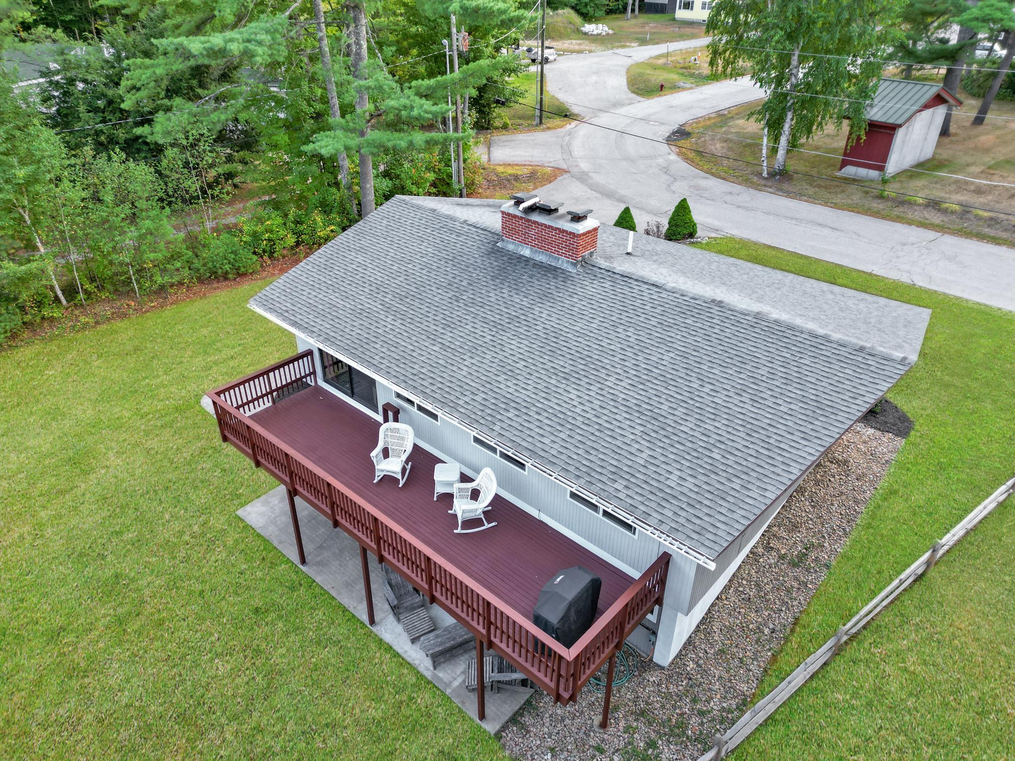 Aerial view of a home with a large red-railed deck overlooking a green lawn and wooded surroundings.