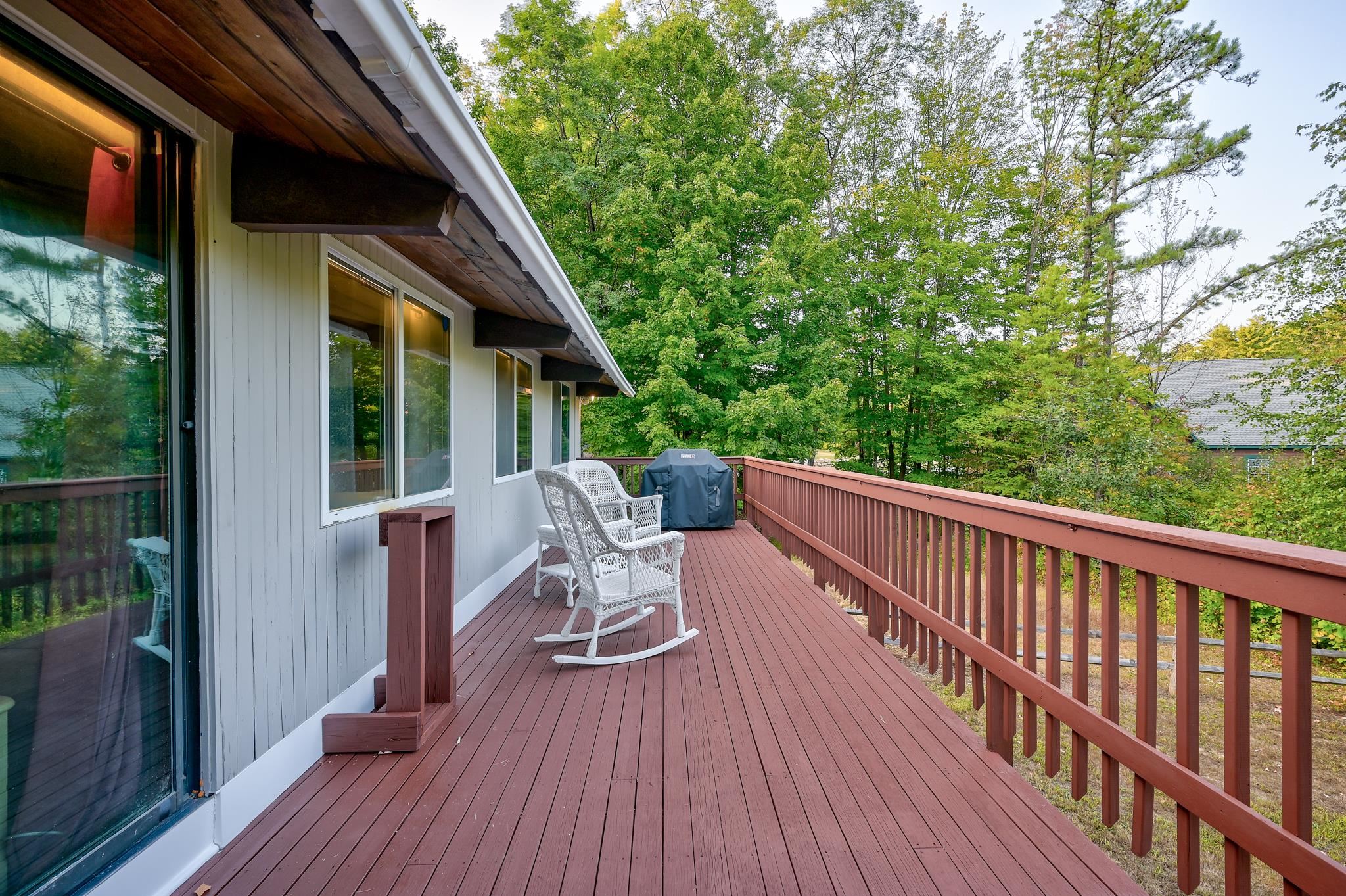 House deck with white rocking chairs, a covered grill, and a leafy wooded view.