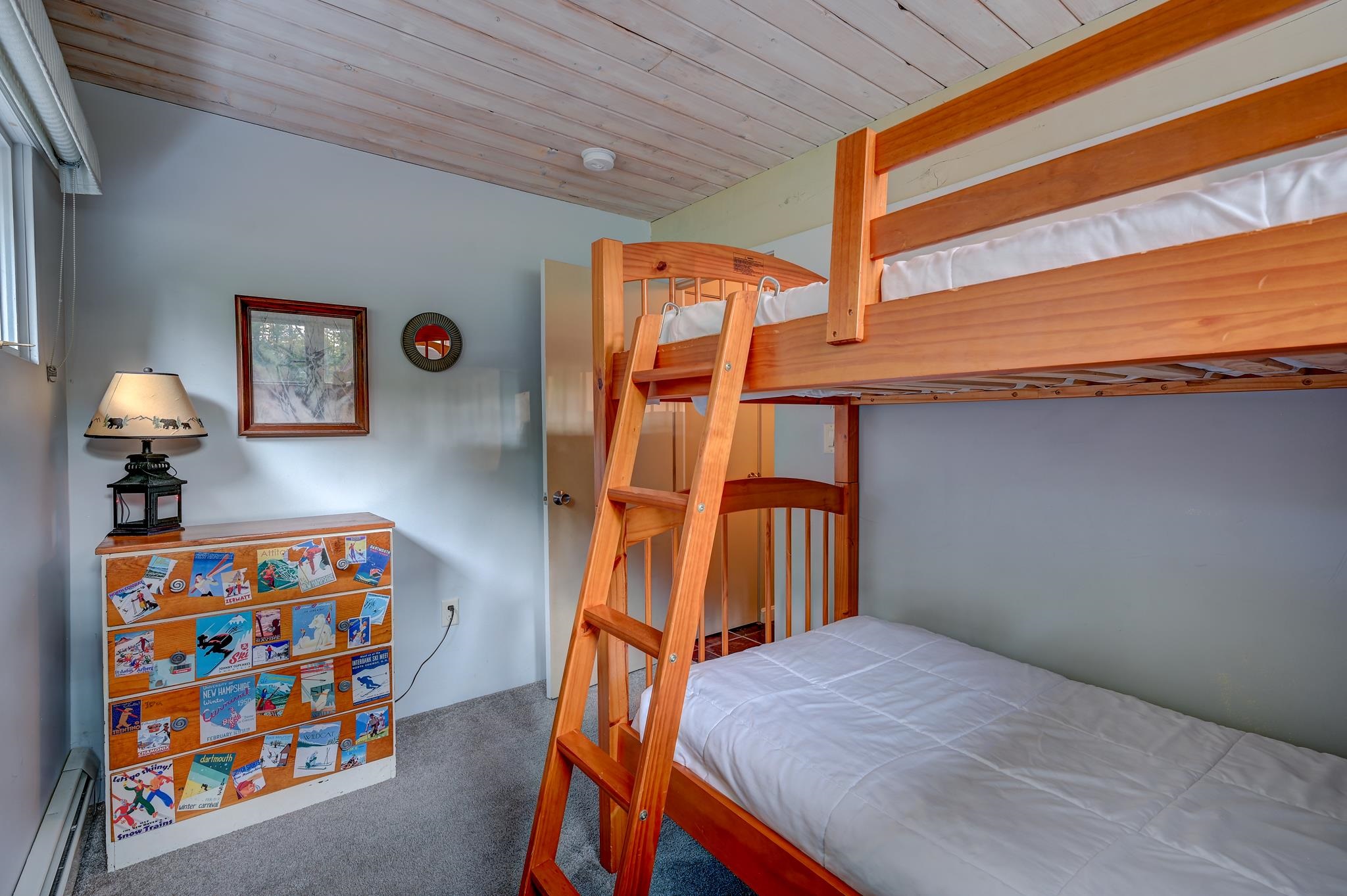 Bedroom with a wooden bunk bed, white bedding, and a sticker-covered dresser.