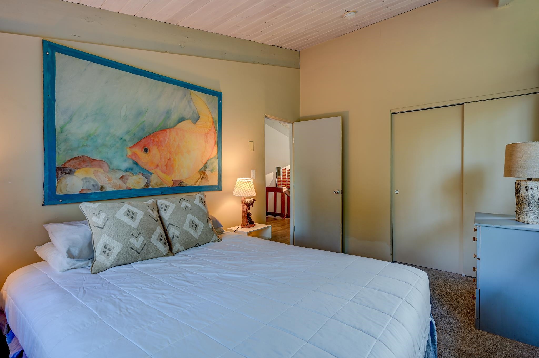 Bedroom with a white quilted bed and a large colorful fish painting above it.