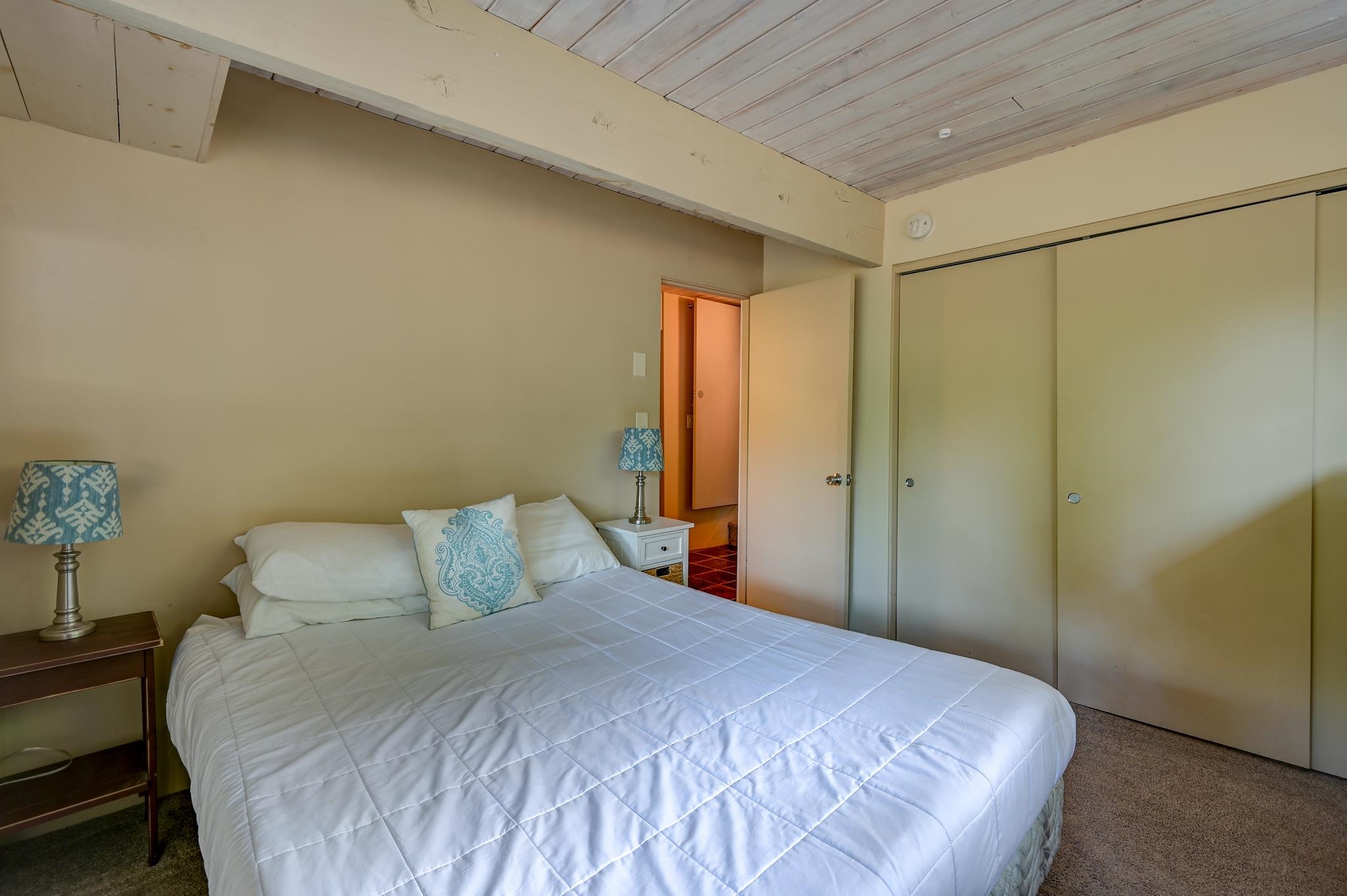 Bedroom with a white quilted bed, blue-patterned pillows, and a sloped plank ceiling.