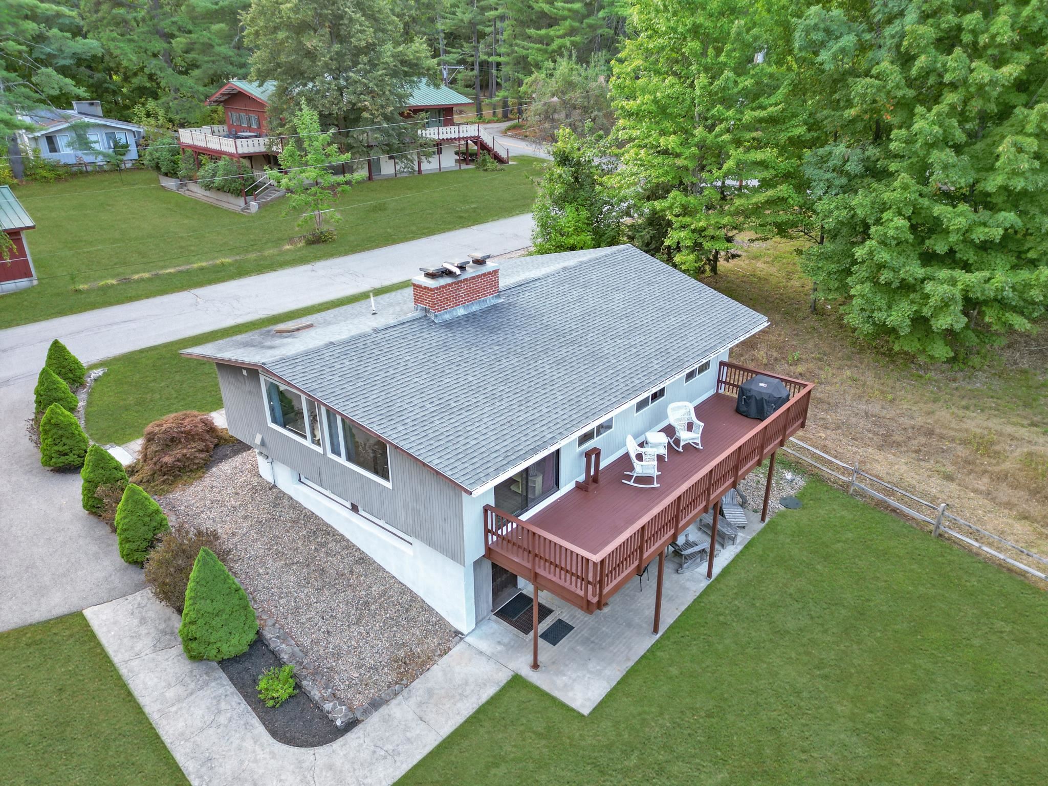 Aerial view of a gray split-level home with a spacious raised deck and white patio chairs.