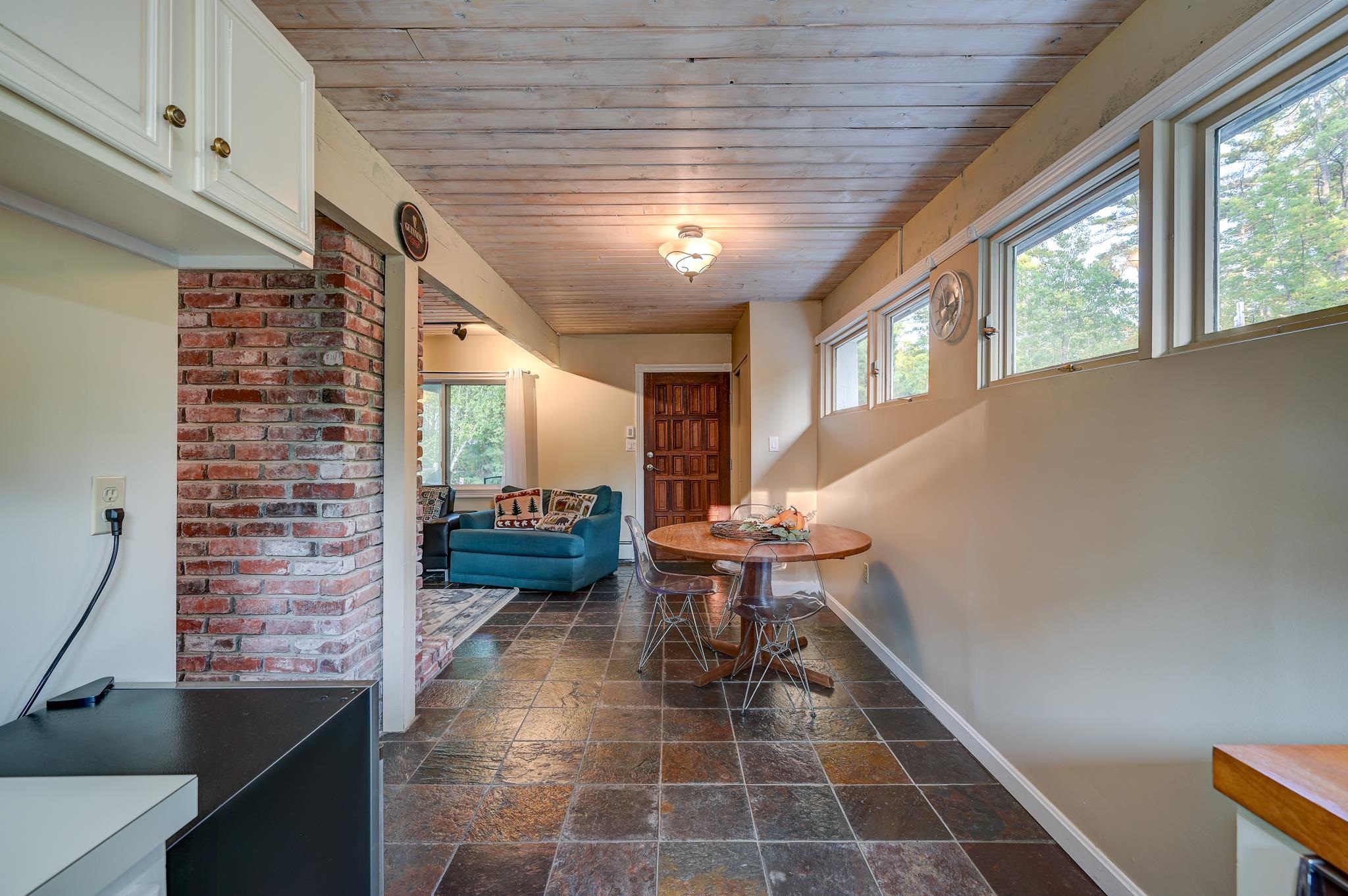 Dining area with a round wooden table, dark tile floor, brick pillar, and windows.
