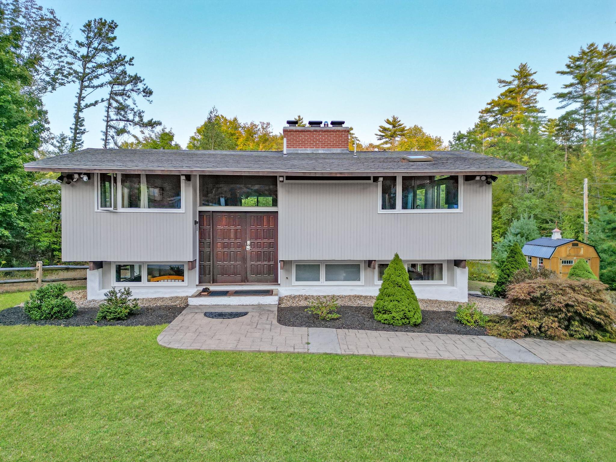Gray split-level house with dark double doors, a brick chimney, and a paved front walkway.