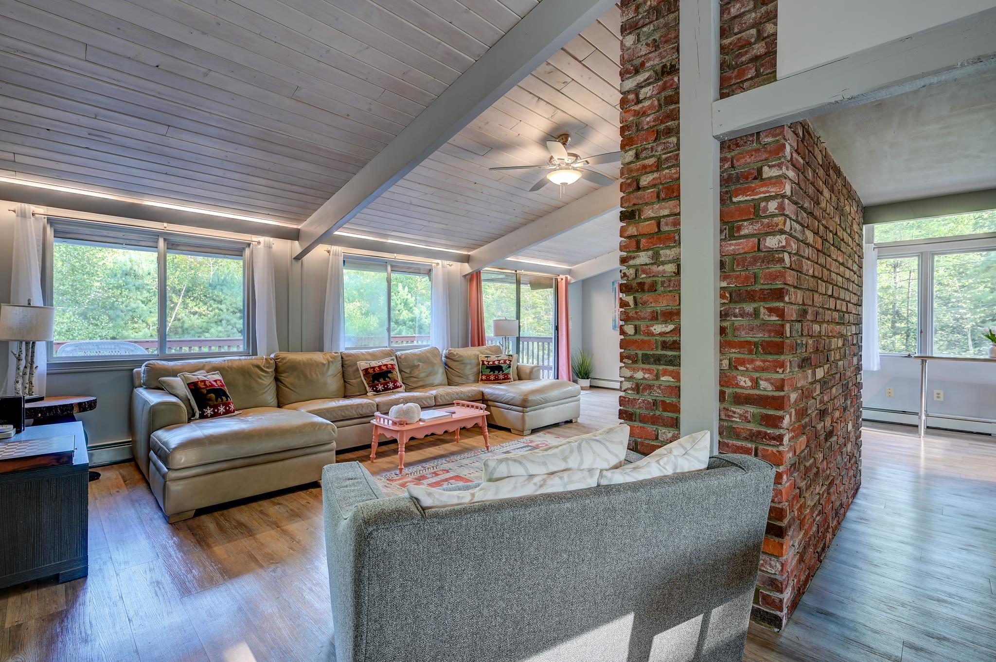 Living room with a vaulted plank ceiling, brick chimney, large windows, and two sofas.