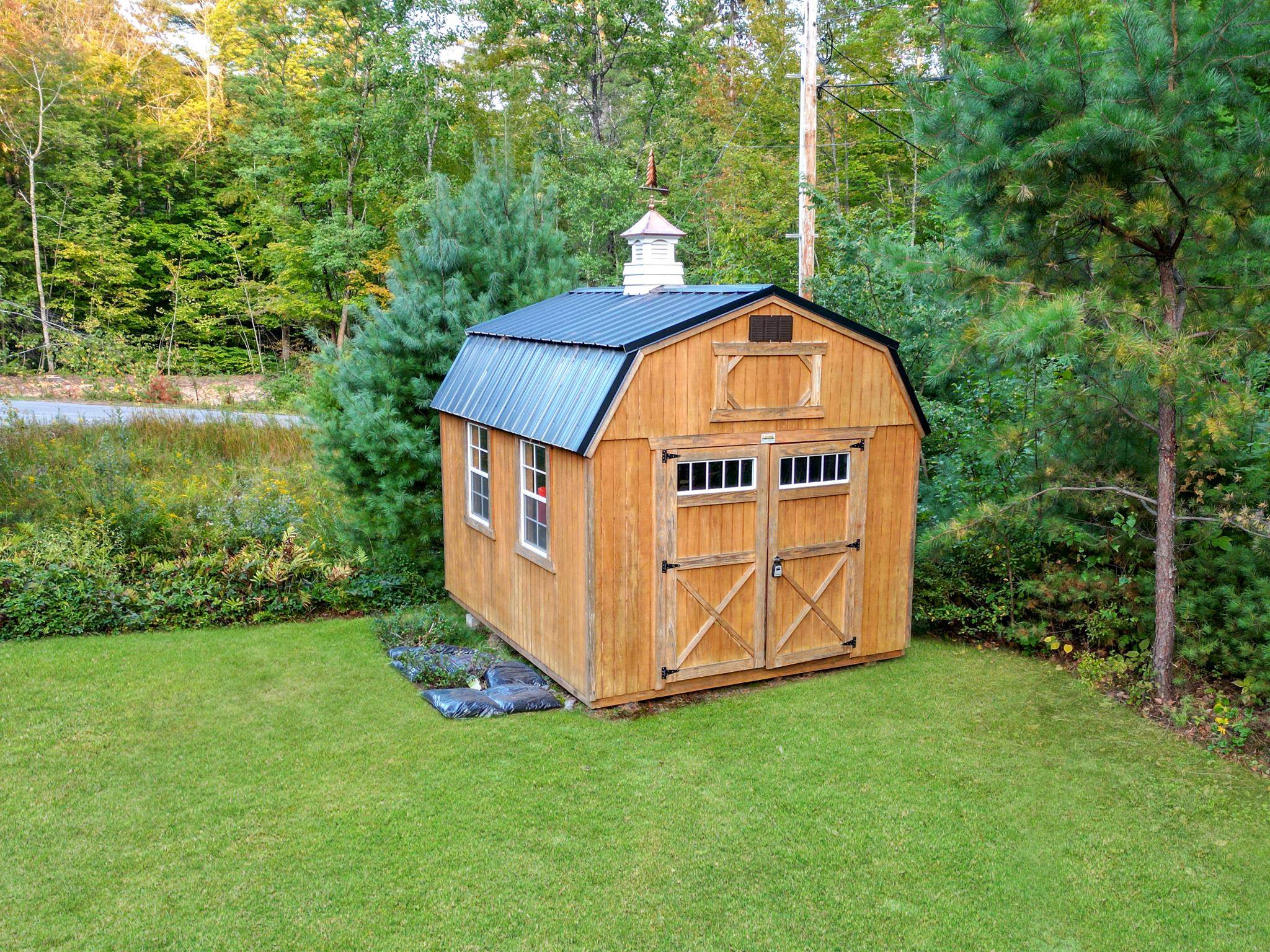 Wooden storage barn with double doors and cupola on a lawn amid trees.
