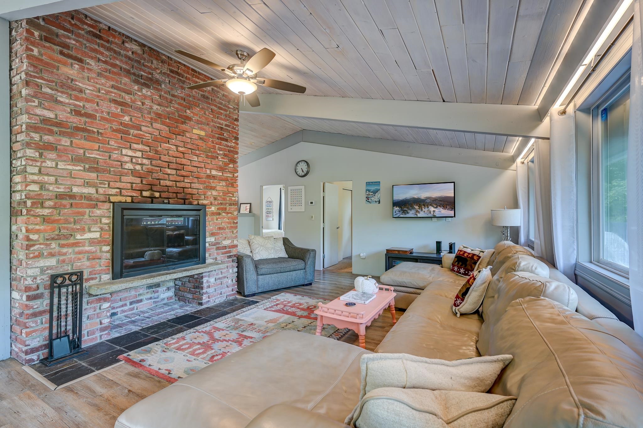 Living room with a brick fireplace, vaulted ceiling, and beige sectional beside large windows.
