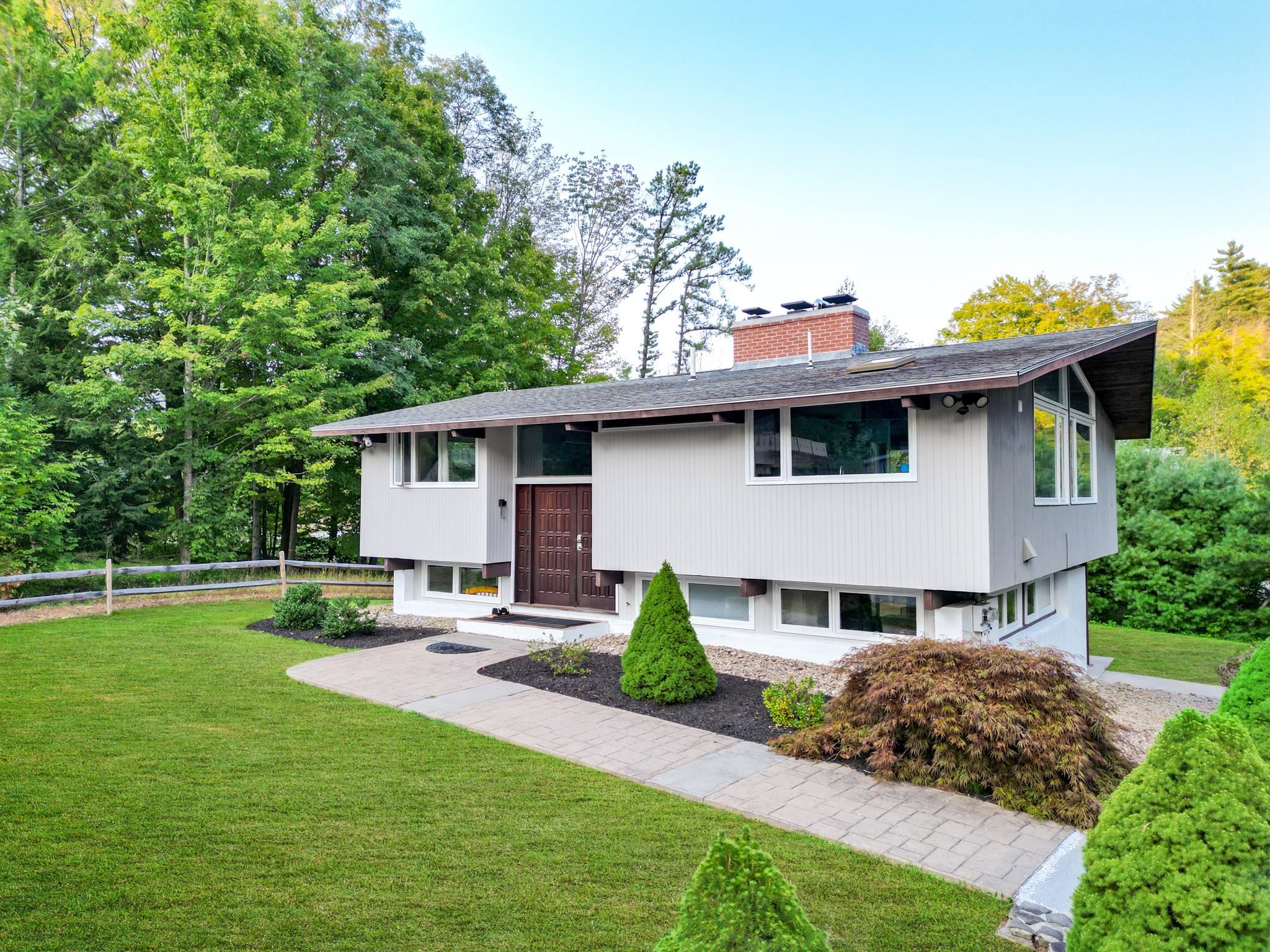 Modern split-level home with white siding, landscaped garden beds, and a paved walkway across the front lawn.