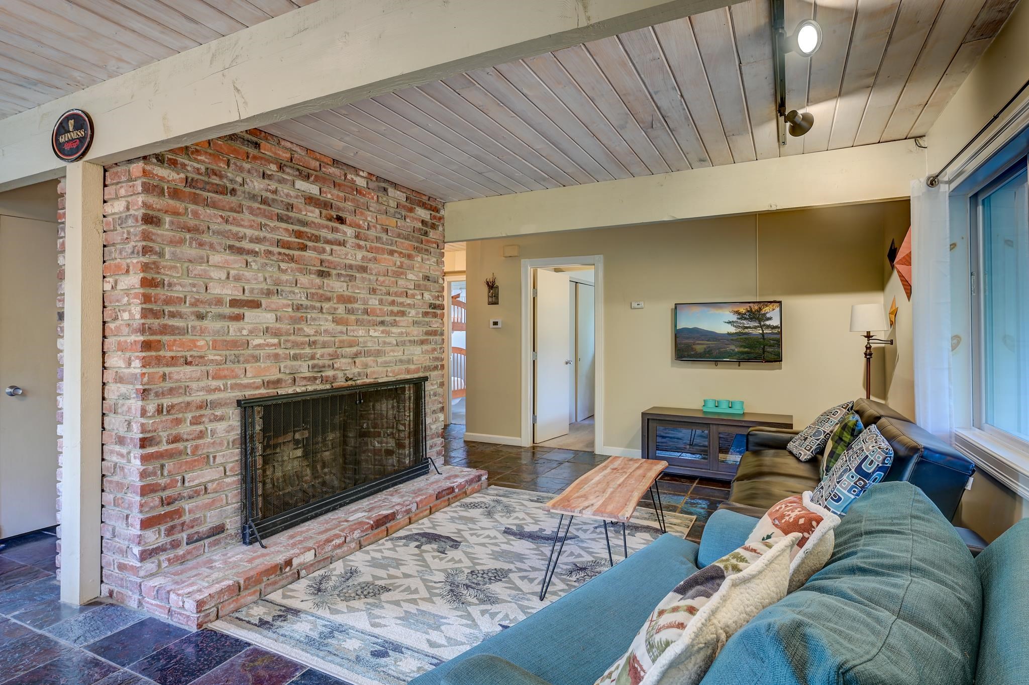 Living room with a brick fireplace, vaulted wood ceiling, slate floor, and blue sofas.