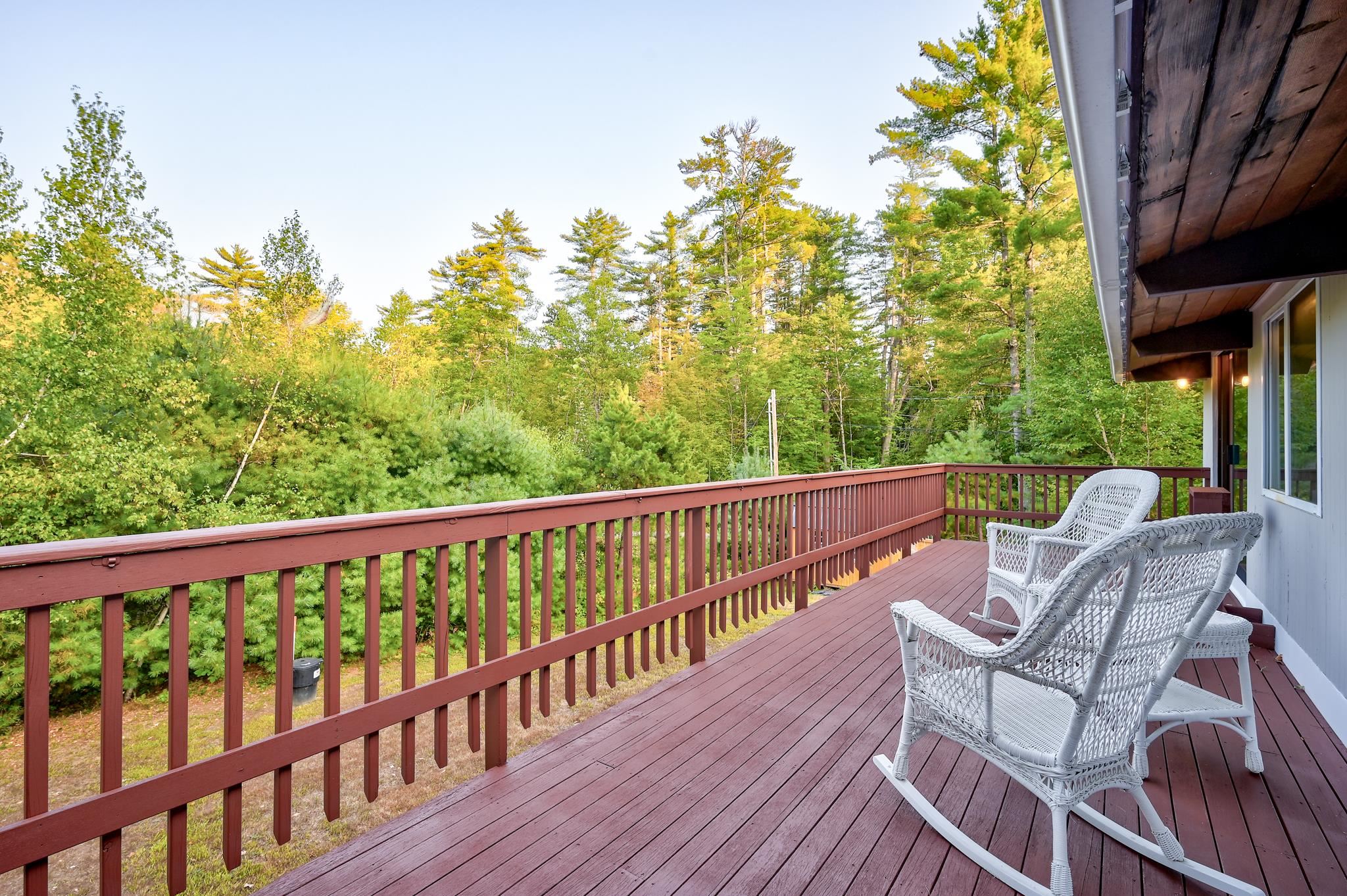 Wooden deck with white wicker rocking chairs overlooking autumn trees.