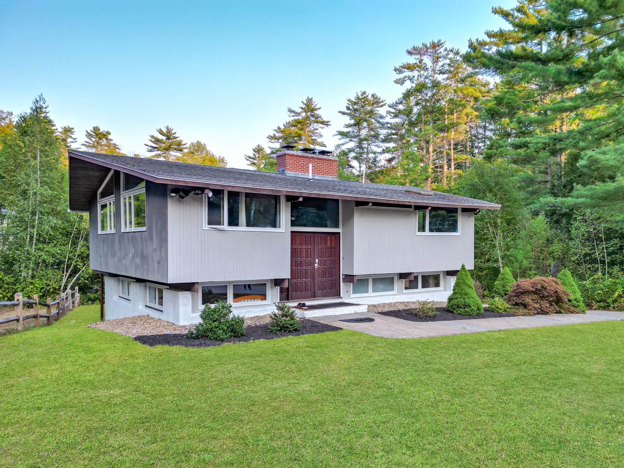 Modern split-level home with broad windows and red double doors, surrounded by lawn and tall trees.