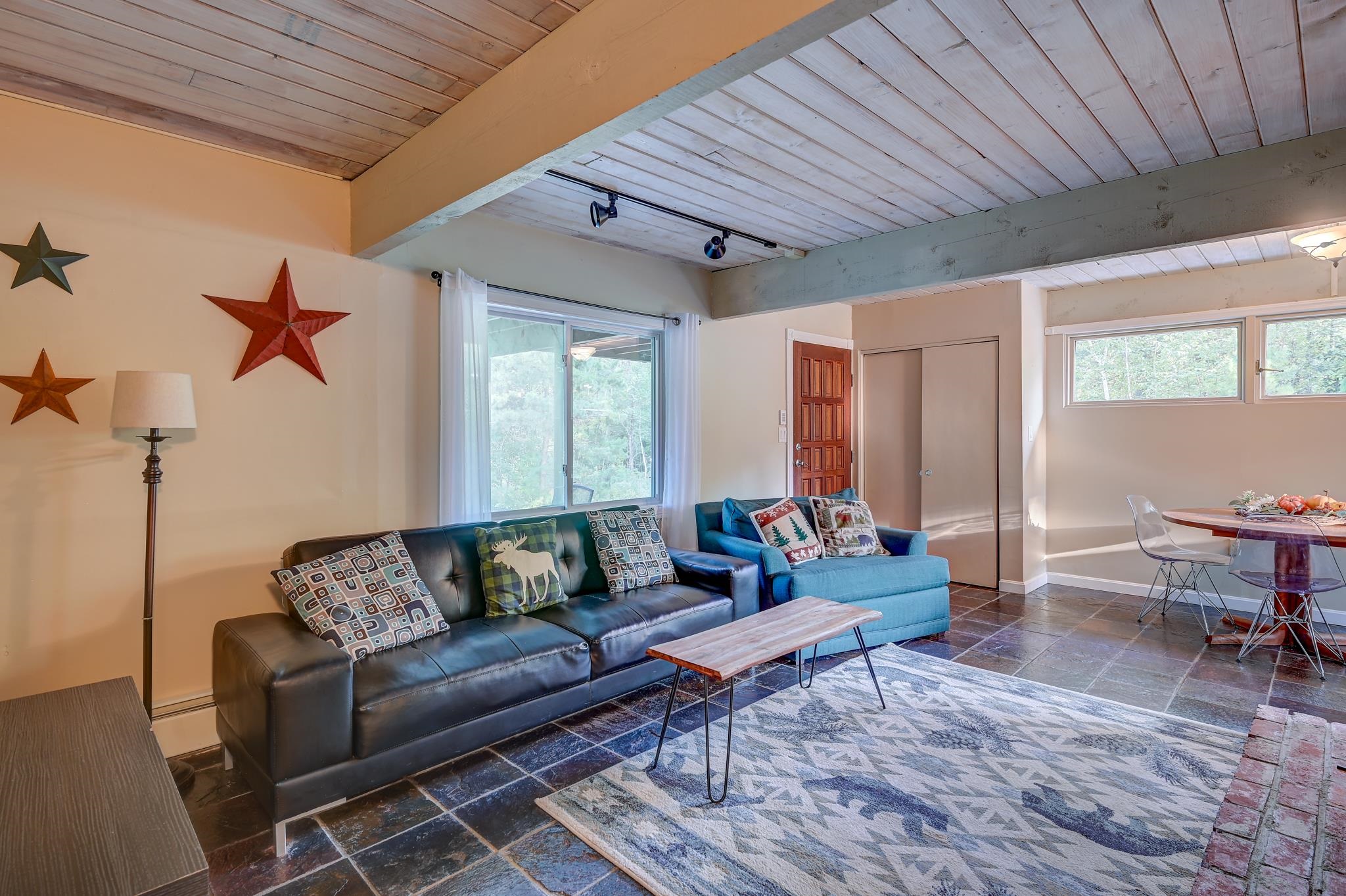 Furnished living room with exposed beams, leather and blue sofas, and an adjacent dining area.
