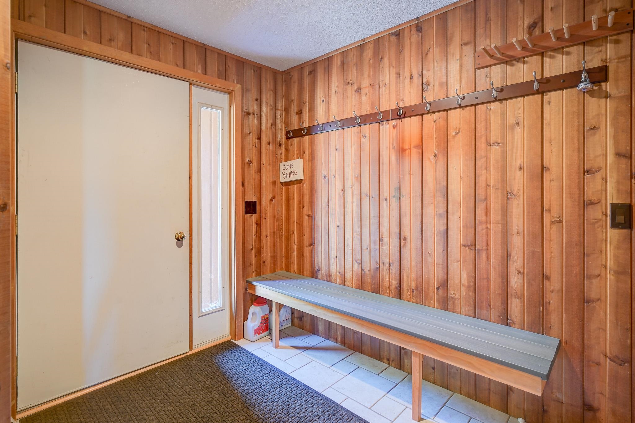 Ski-entry mudroom with wood-paneled walls, a long bench, and rows of hooks.