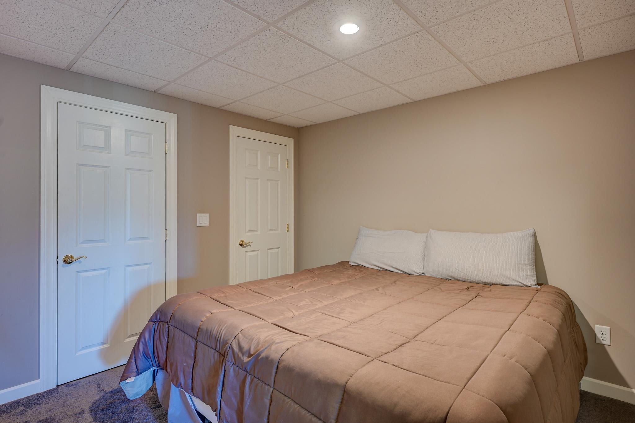 Bedroom with a large taupe-quilted bed, white pillows, beige walls, and two paneled doors.