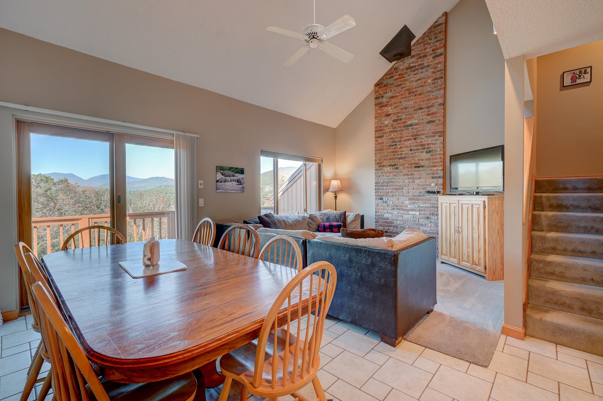 Open-plan living and dining room with a brick fireplace and mountain views through sliding glass doors.