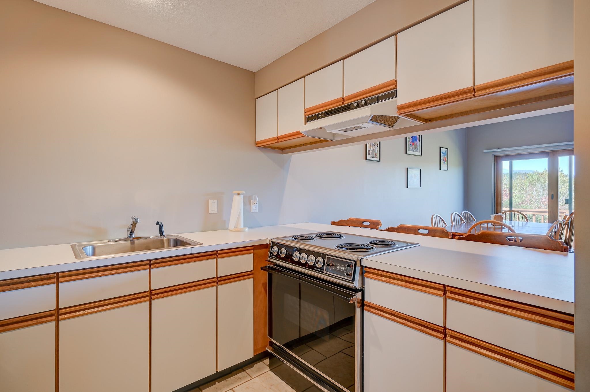 Kitchen with white cabinets and wood trim, an electric range, and dining area by sliding glass doors.