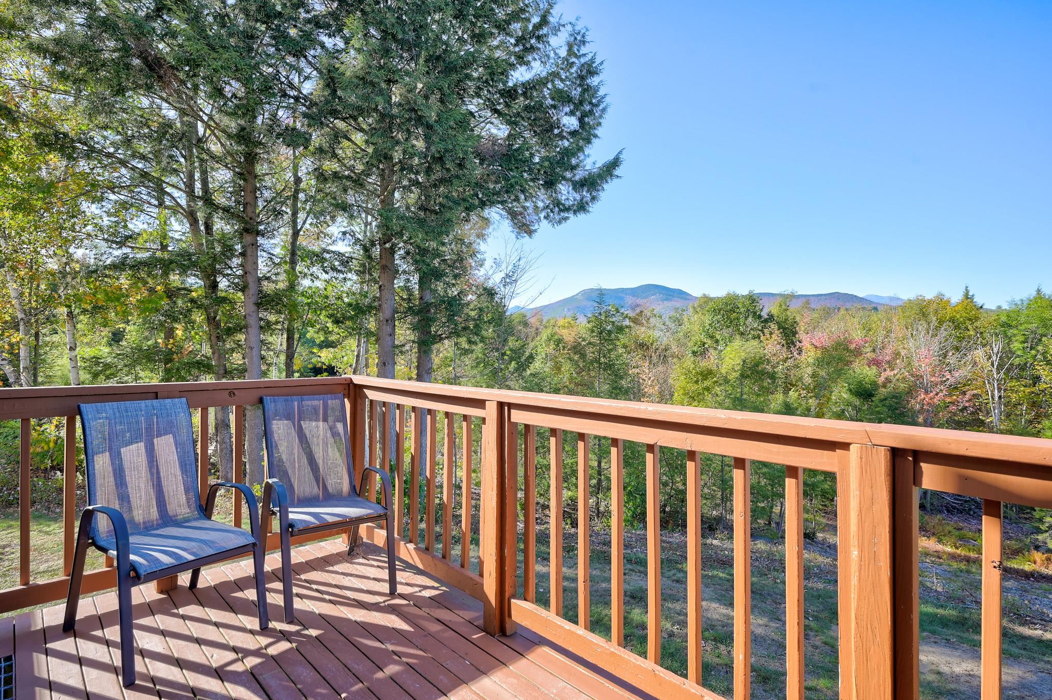 Wooden deck with two blue chairs overlooking autumn woods and distant mountains.