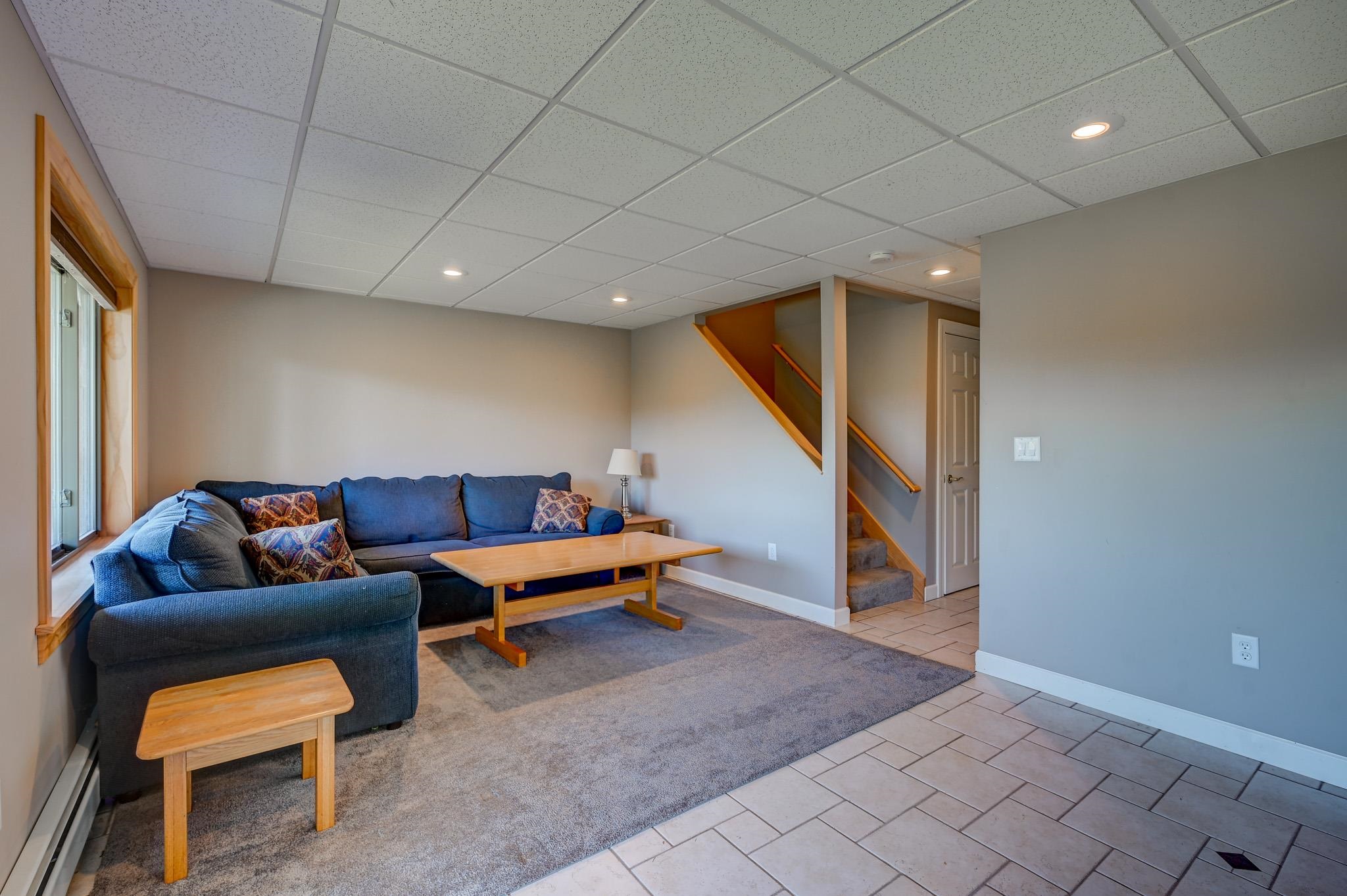 Basement living room with a blue sectional, wooden coffee table, and stairs.