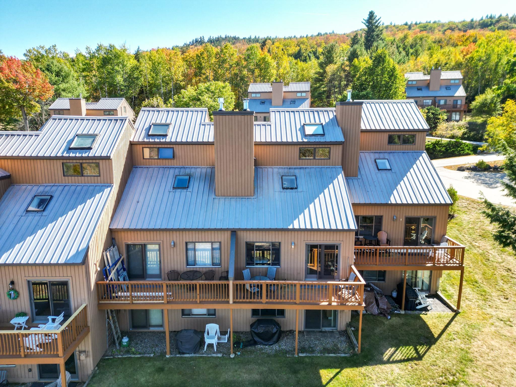 Aerial view of brown townhomes with metal roofs and decks beneath autumn-colored hills.