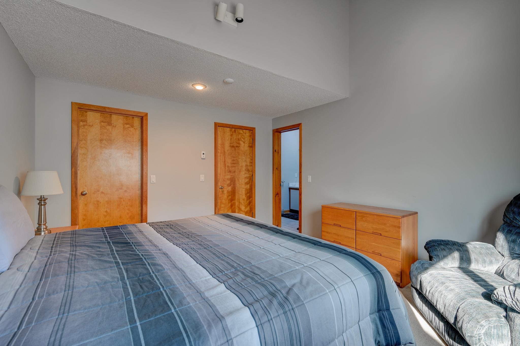 Bedroom with blue plaid bedding, wooden dresser, and an open doorway to the bathroom.