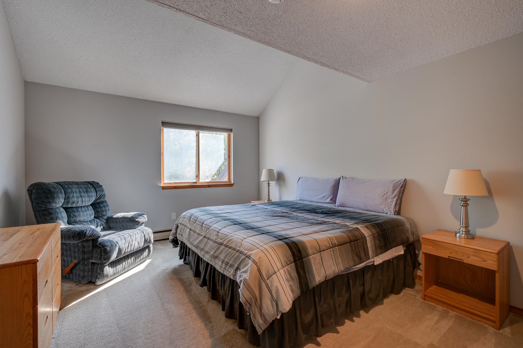 Furnished bedroom with a large plaid-covered bed, blue recliner, and window.